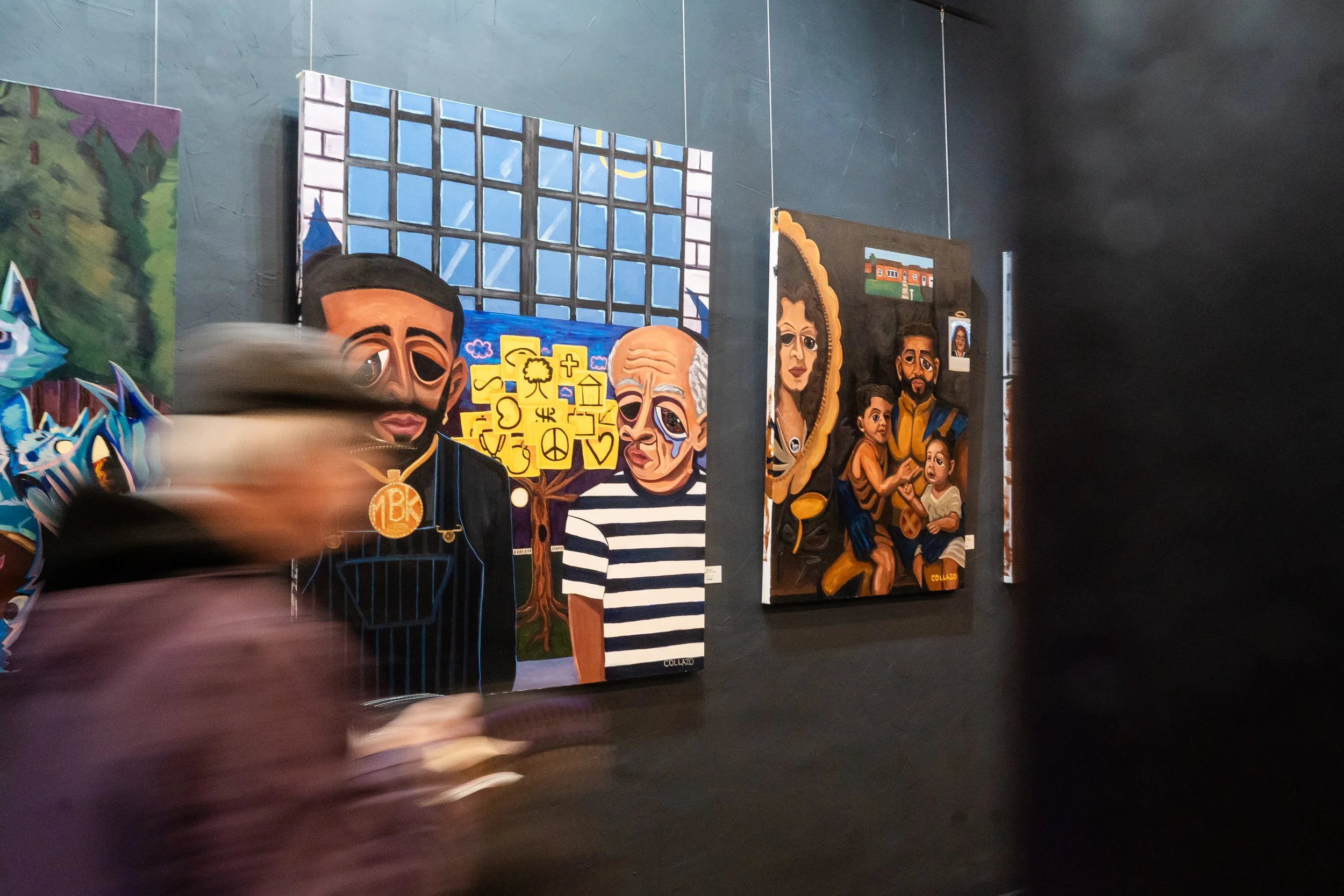 Blurred person walking past colorful paintings in an art gallery with dark walls.