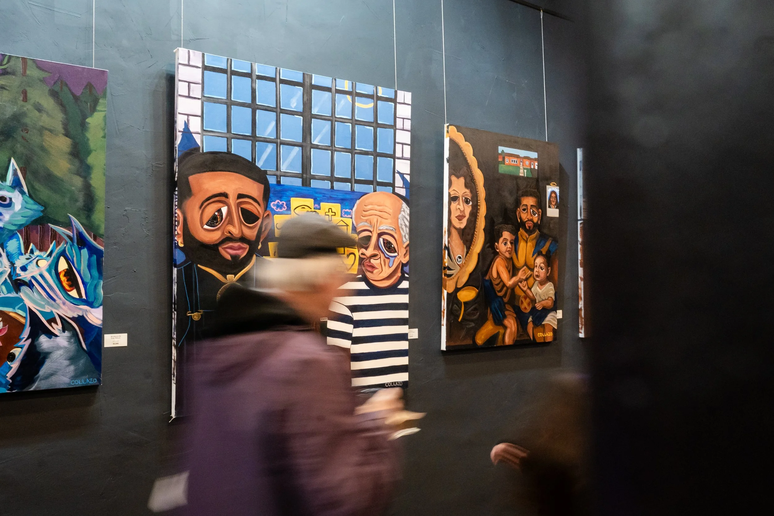 People walking in front of artwork in an art gallery. The paintings feature stylized faces and vibrant colors.