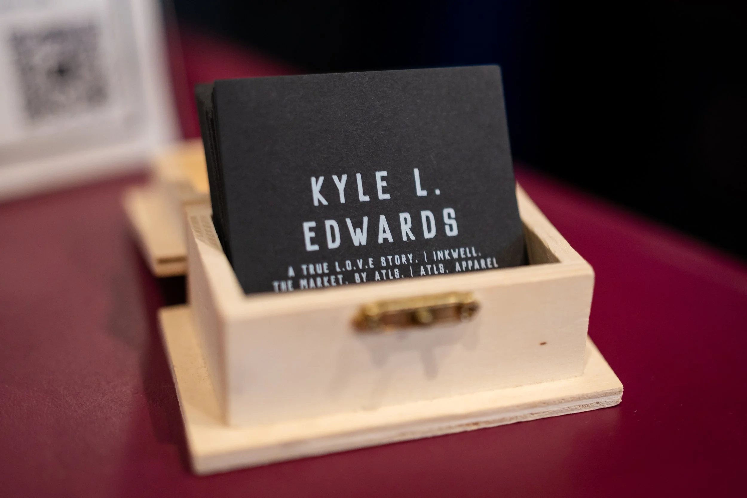 Business card placed inside a small wooden box on a red surface.