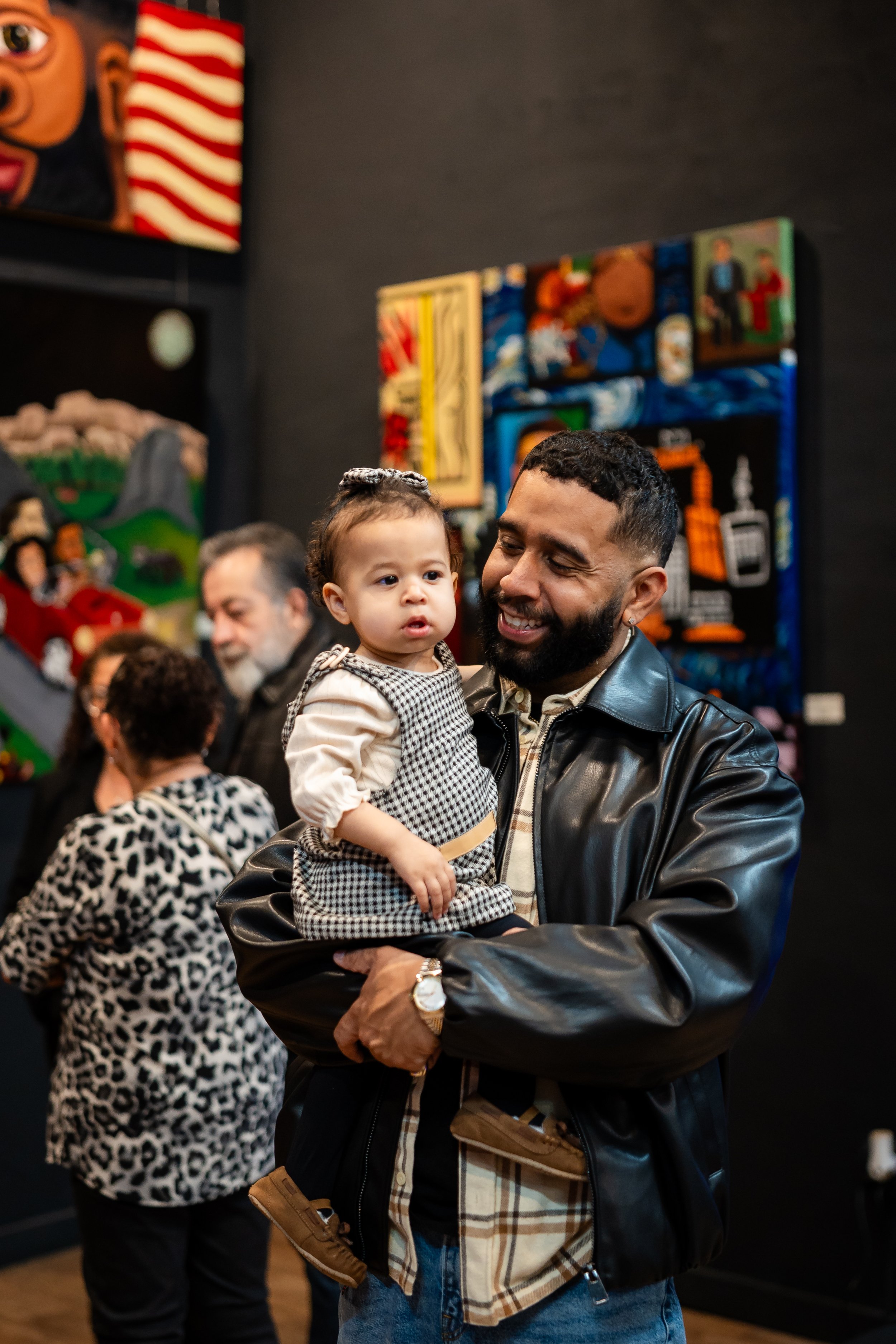 A man holding a young girl at an art gallery with colorful paintings on the wall.