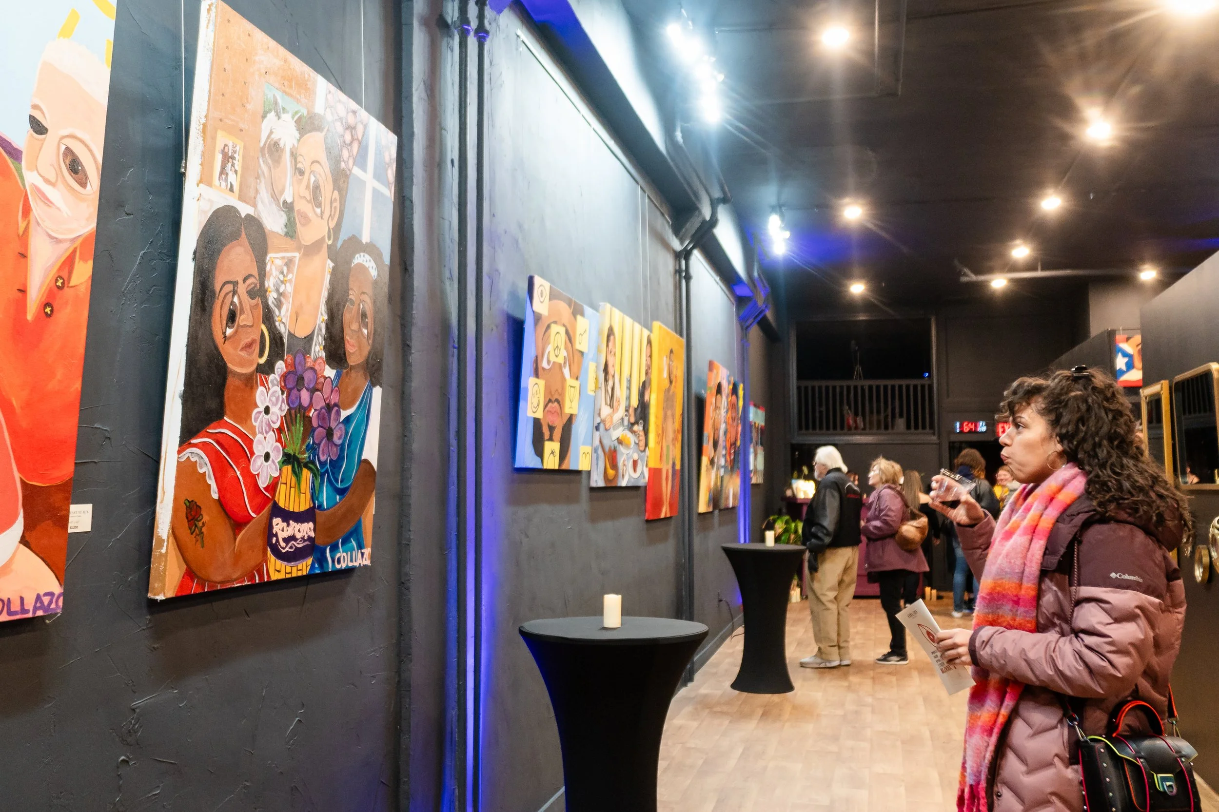 A woman in a brown coat and colorful scarf looking at artwork on display in an art gallery.
