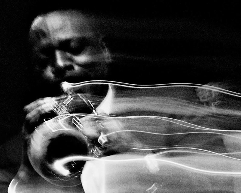 Black and white photo of a person holding a camera, with light trails creating a blurred effect.