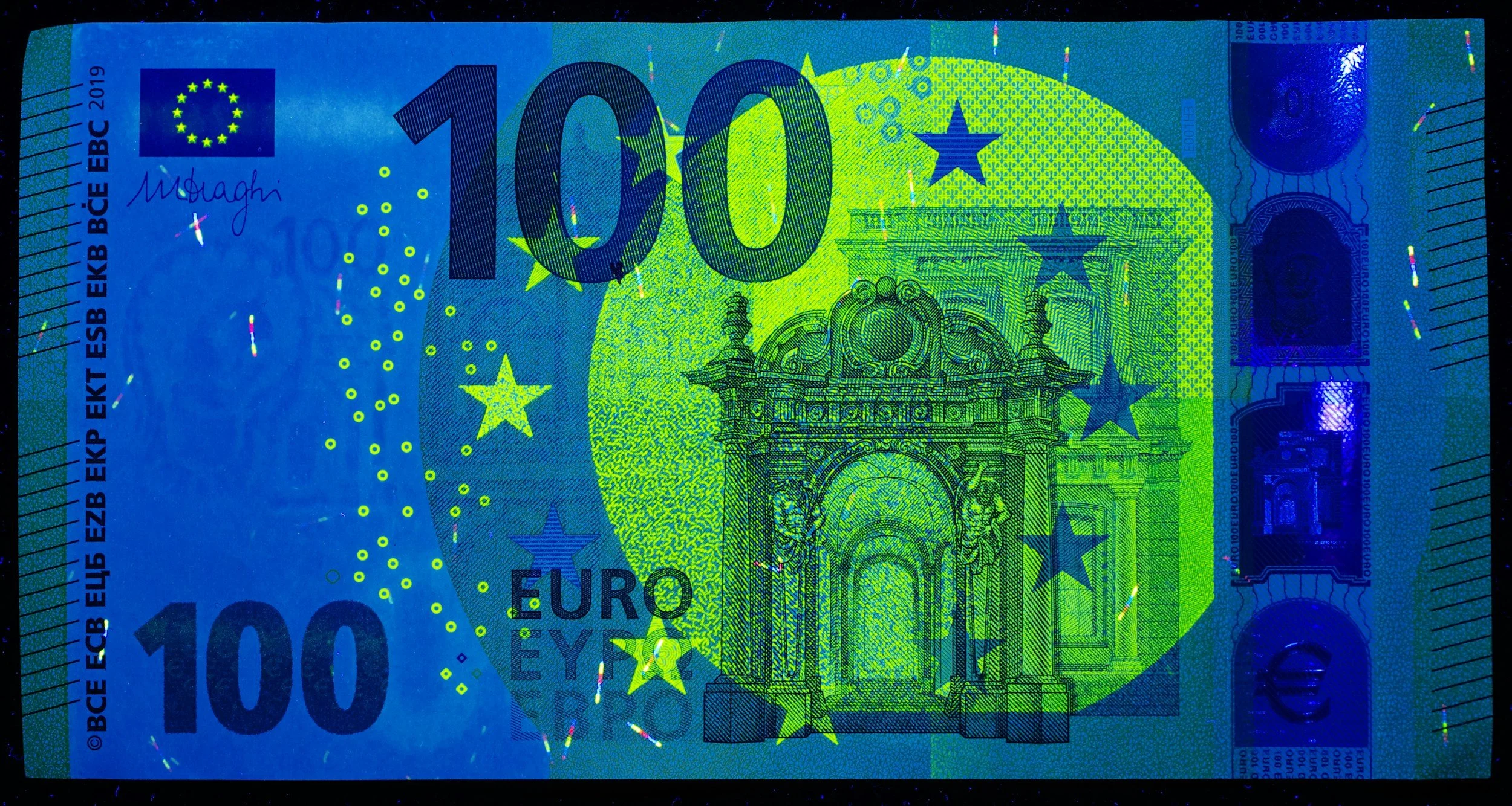 Close-up of a 100 euro banknote with detailed design elements, including the euro symbol, number, and architectural illustration in green and blue colors.