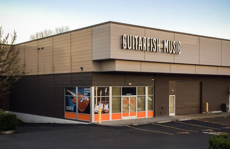 Exterior of Guitarfish Music store with large sign, glass windows displaying guitars, and a parking lot in front.