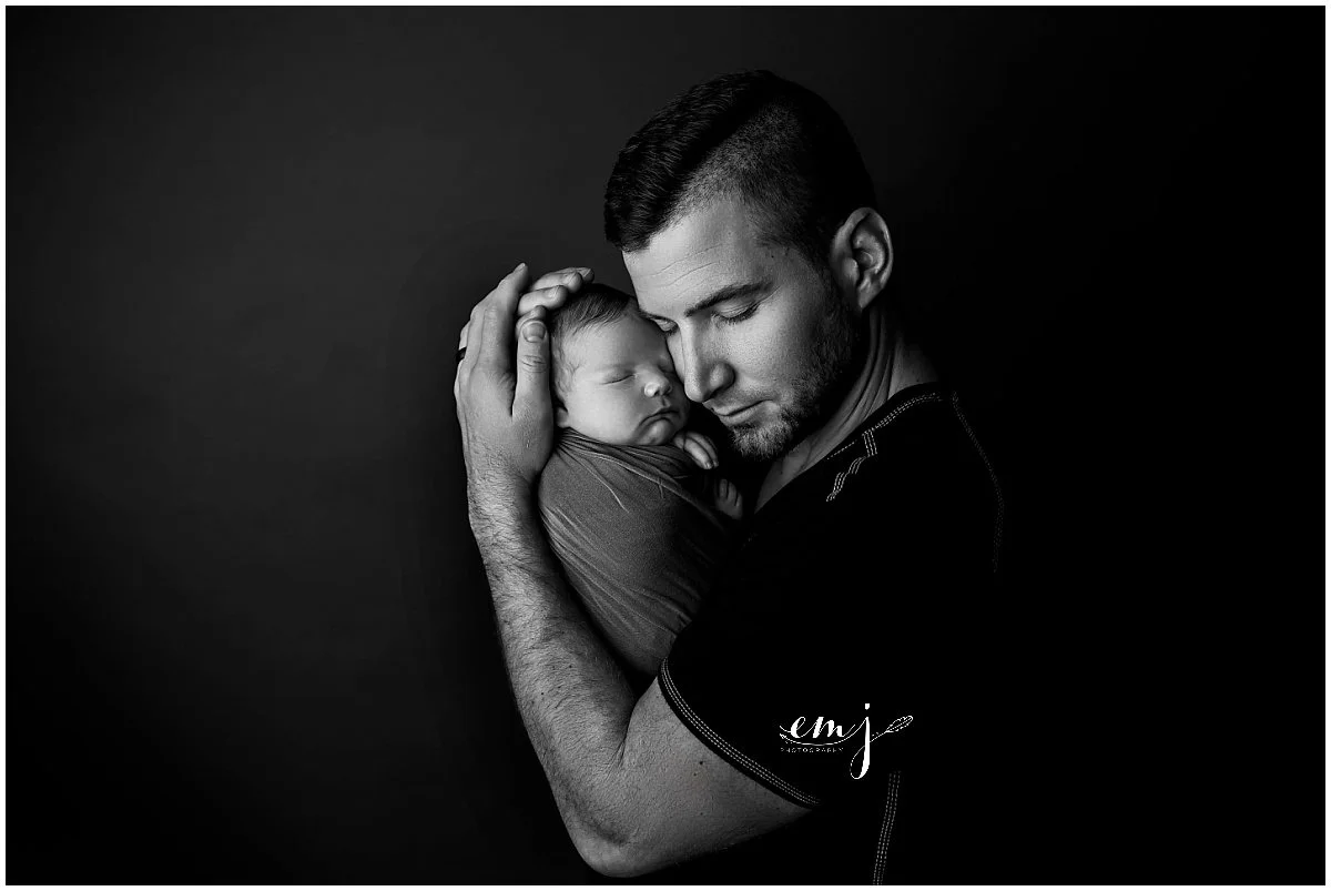 Father holding his sleeping newborn baby during a studio newborn photography session in Syracuse, Utah