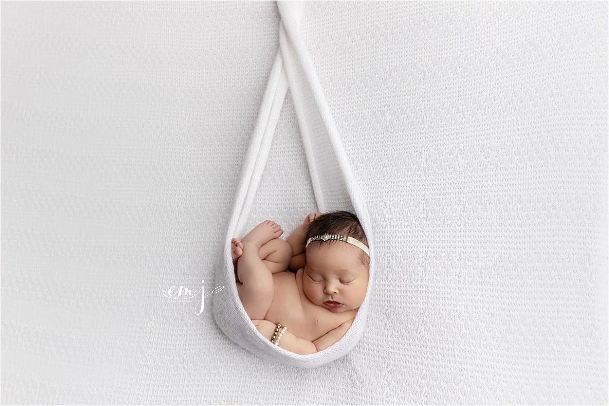 Sleeping newborn baby posed in a white hanging sling during a studio newborn photography session in Syracuse, Utah