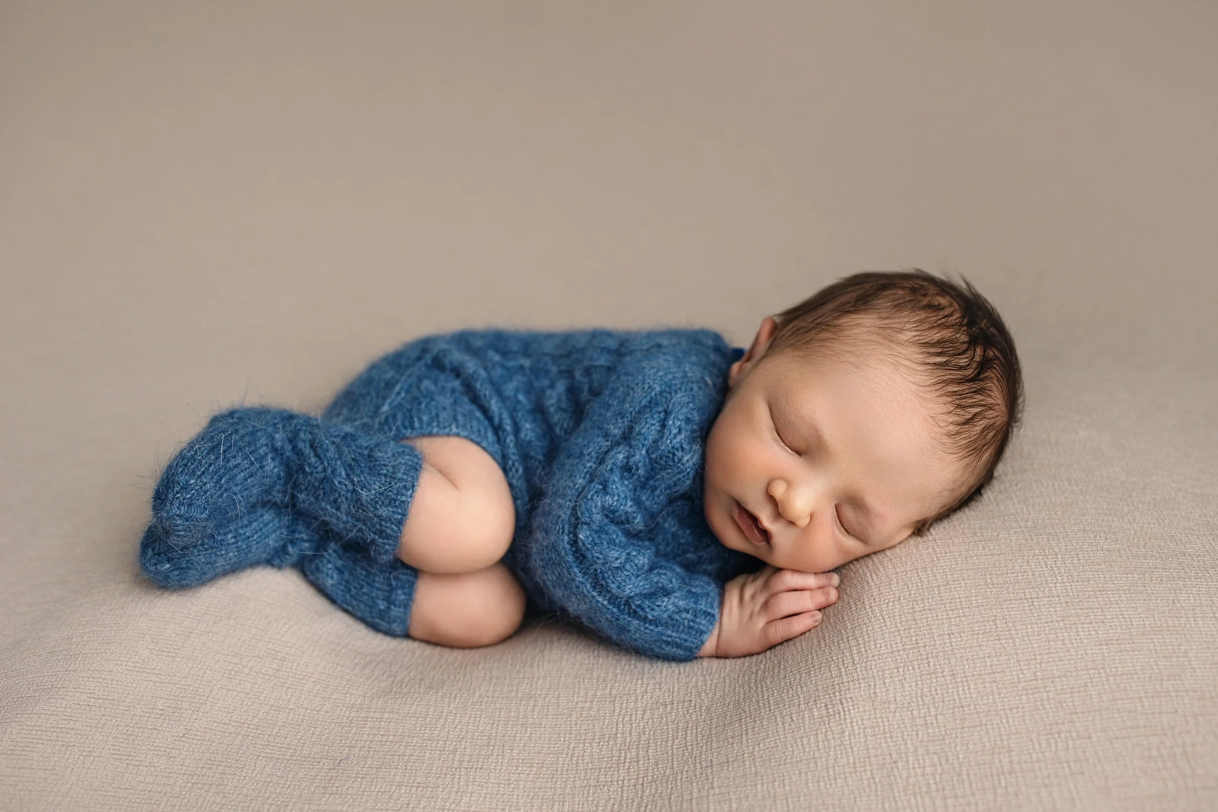 Sleeping newborn baby in a blue knit outfit during a studio newborn photography session in Syracuse, Utah.