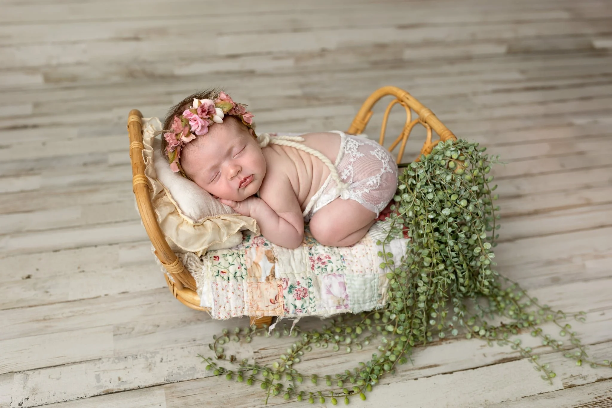 Sleeping newborn baby girl wearing a pink floral headband, posed in a wicker basket during a studio newborn photography session in Syracuse, Utah.