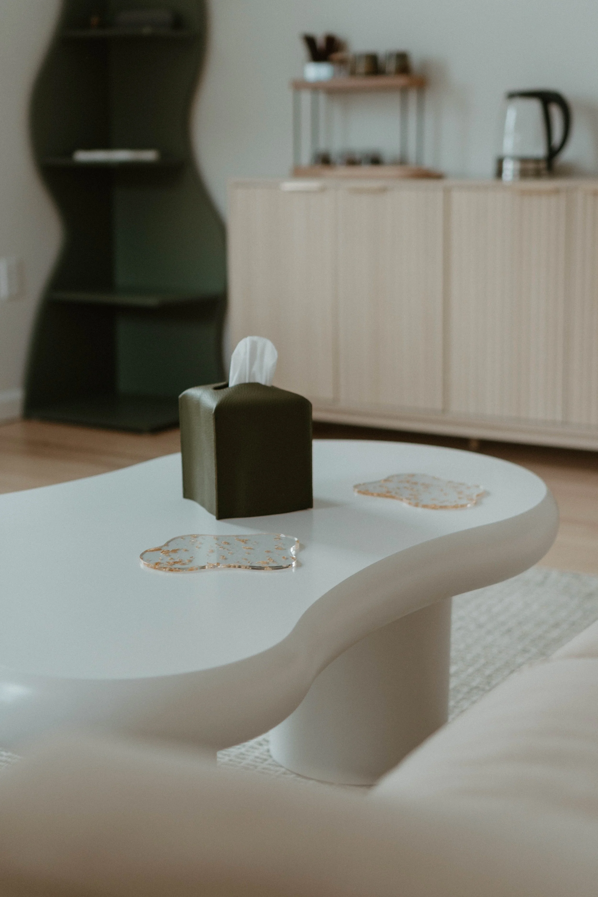 A white coffee table with a black tissue box and two decorative glass coasters in a modern living room.