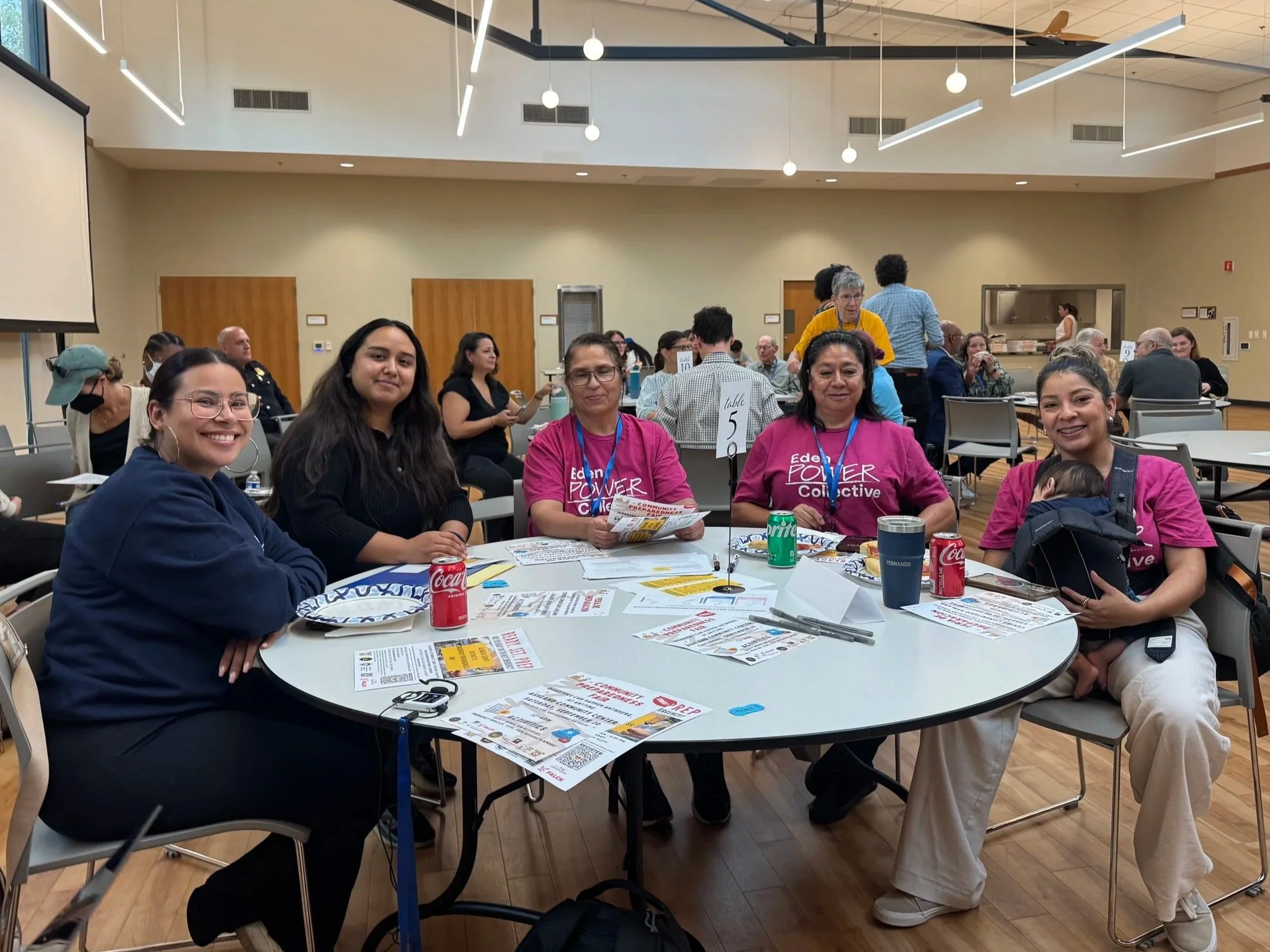 People smiling at a table, some of them wearing Eden Power Collective shirts