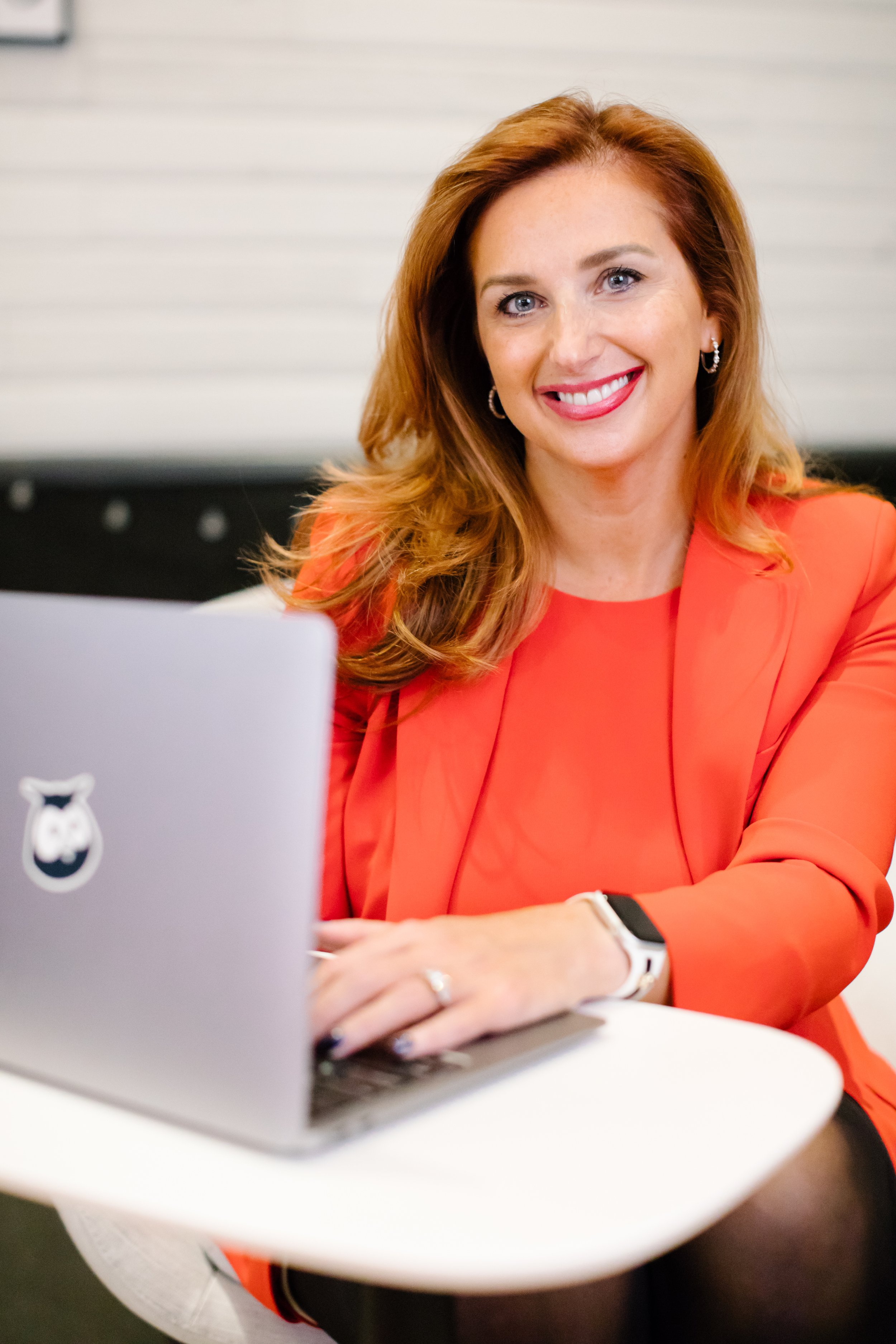 Woman in red outfit smiling, sitting at desk with laptop