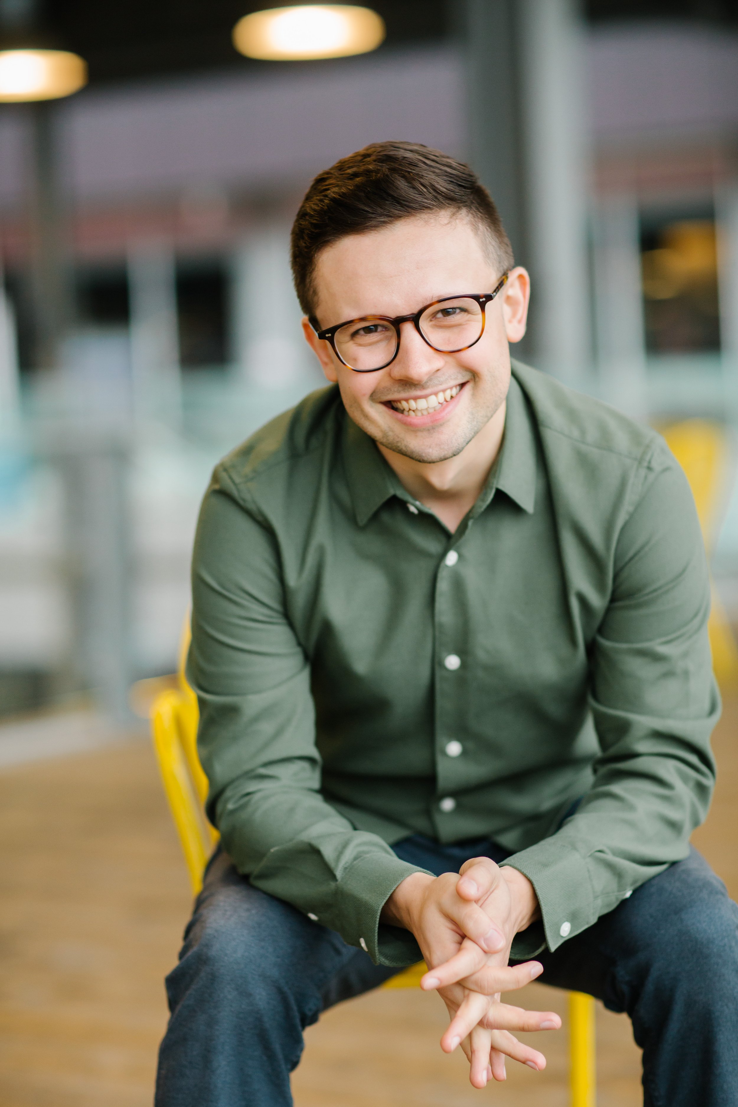 A man wearing glasses and a green shirt, sitting and smiling.
