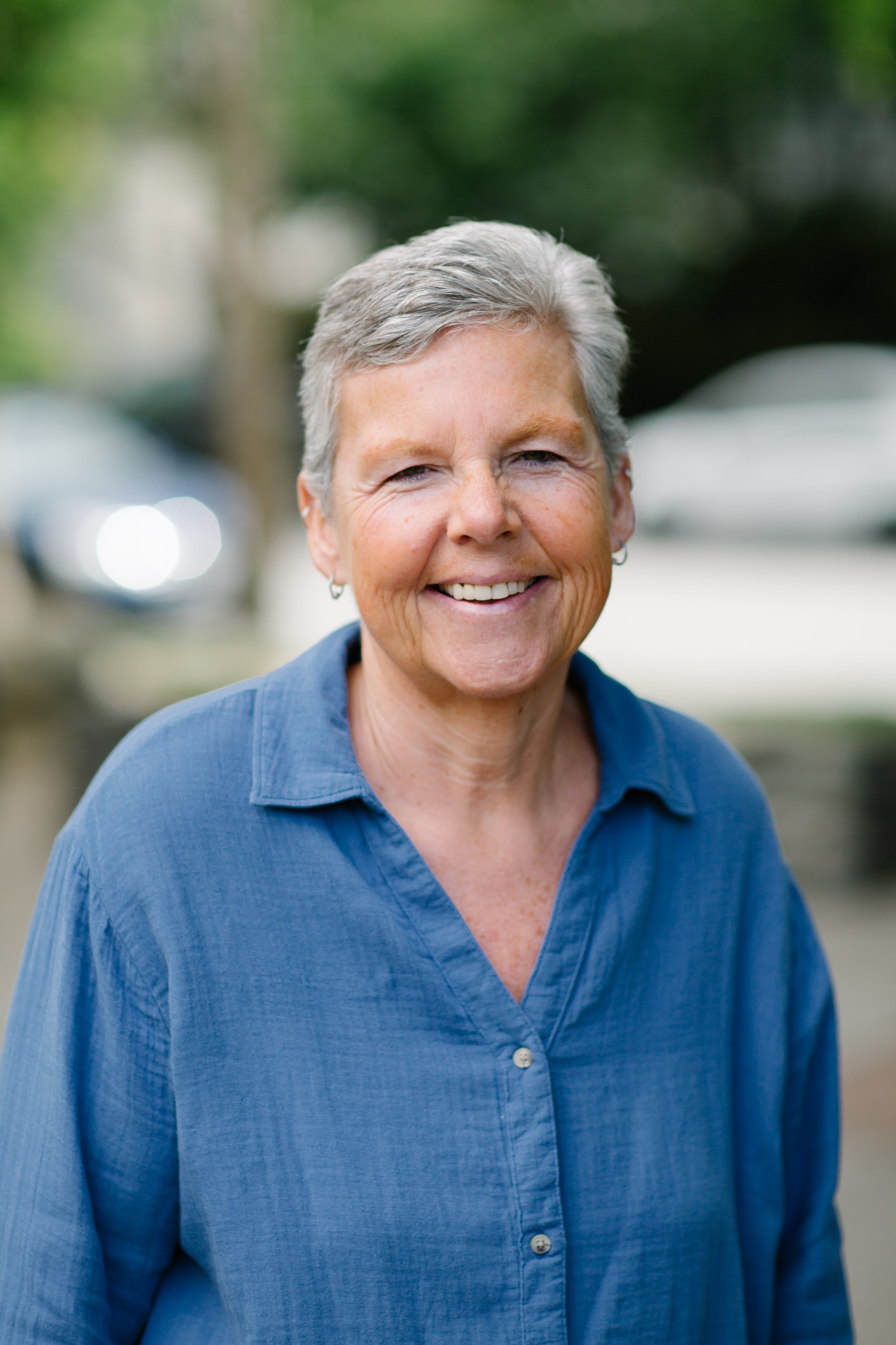 Smiling woman with short gray hair wearing a blue shirt outdoors.