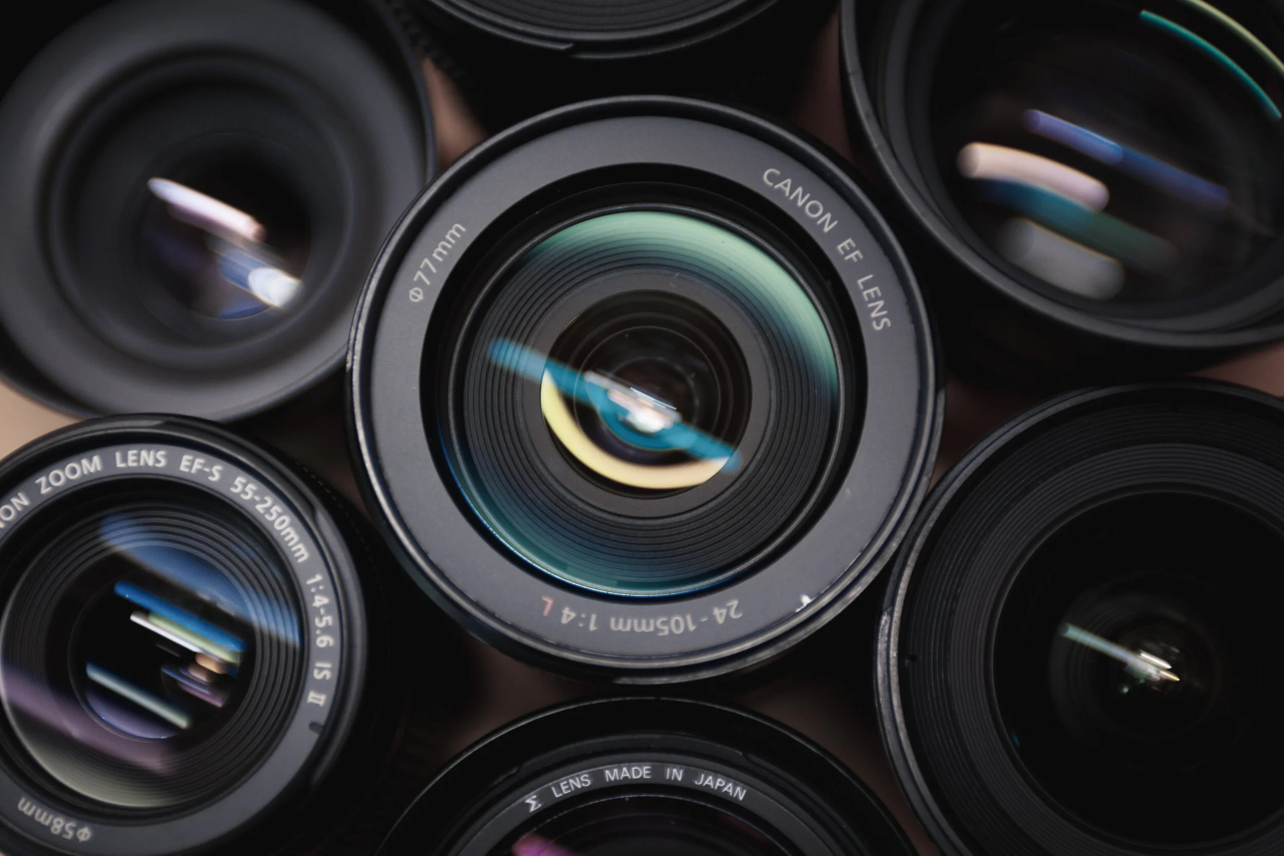 Multiple camera lenses arranged in a cluster, including a Canon EF lens and a zoom lens, with reflections visible on the glass elements.
