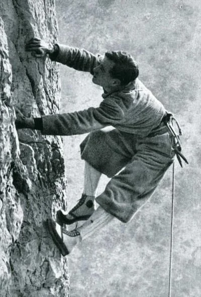 33. Black-and-white photograph of an early rock climber ascending a steep rock face wearing traditional climbing shoes.jpg
