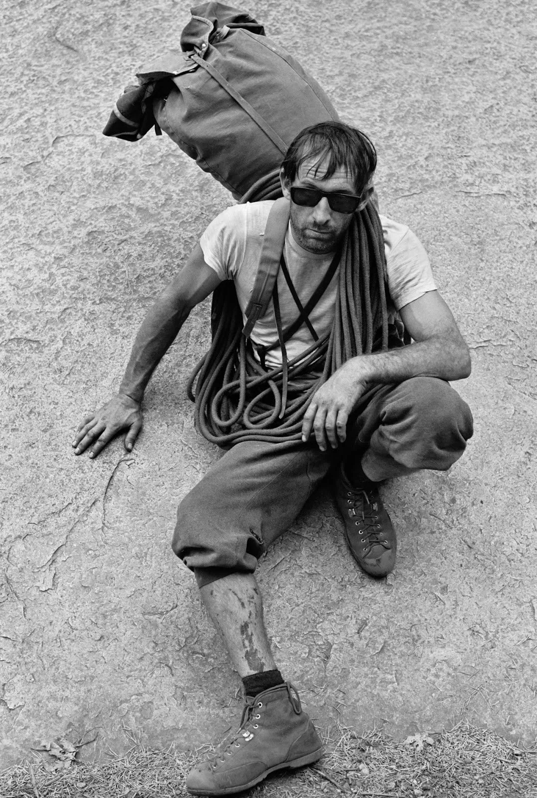 63. Black-and-white photograph of Royal Robbins seated on rock with coiled rope and pack, wearing early climbing boots.jpg