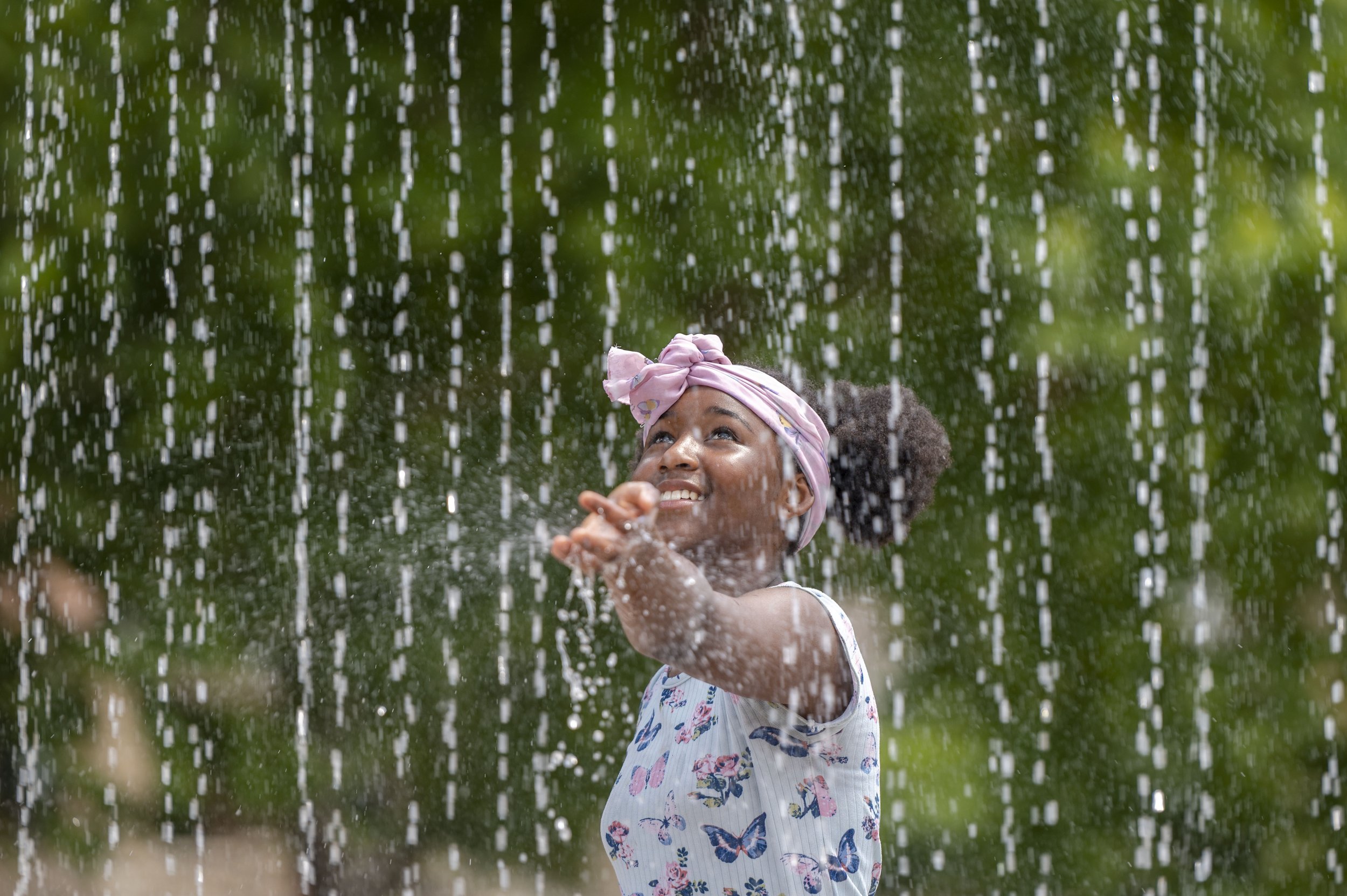  Eleven-year-old Jazya Avery tests the warmth of the water before walking through the fountain at the Sprayground in Gillham Park on Monday, July 18, 2022, in Kansas City.  