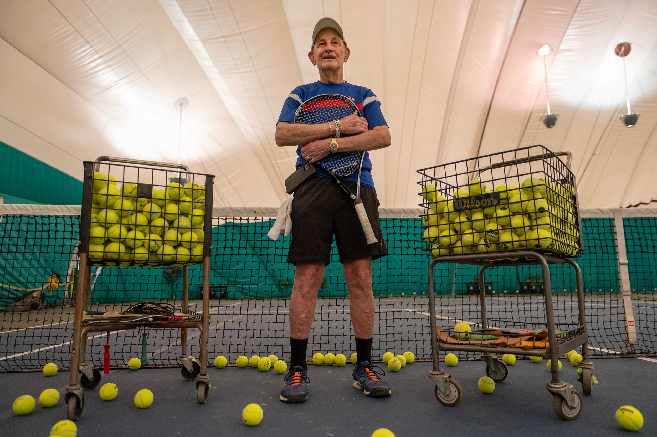  Eighty-year-old Ray Lake holds his tennis racket at Woodside Health and Tennis Club on Monday, March 13, 2023, in Westwood, Kan. A semi-retired psychiatrist, Lake has been competing in United States Tennis Association league matches since the 1970s.