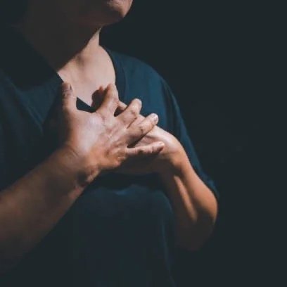 Person holding hands over their heart in a dark setting