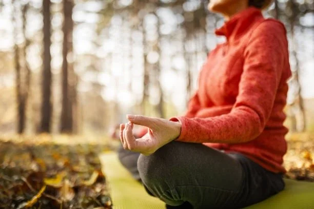 Person practicing meditation outdoors in the woods, connecting to nature, listening to the rhythms of the seasons for better health