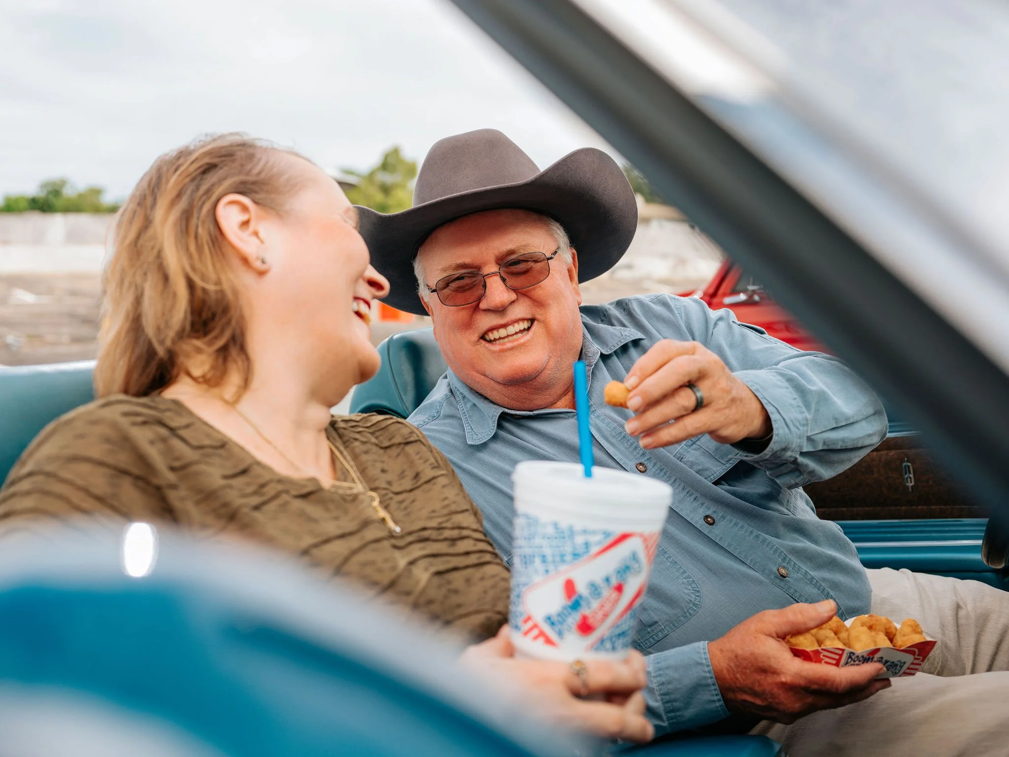 two adults sitting in car enjoying food from Boomarang Diner