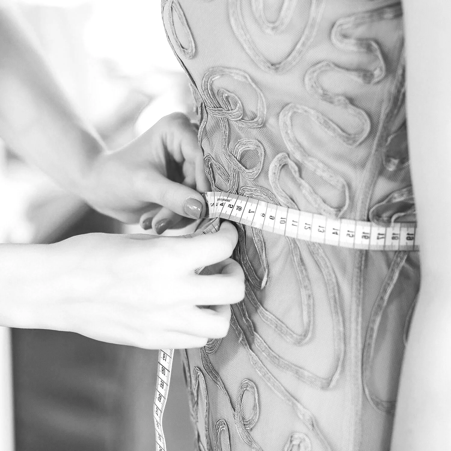 A well-manicured hand skillfully takes measurements of an elegantly embellished gown, capturing the meticulous craftsmanship involved in creating a perfectly tailored and adorned garment.