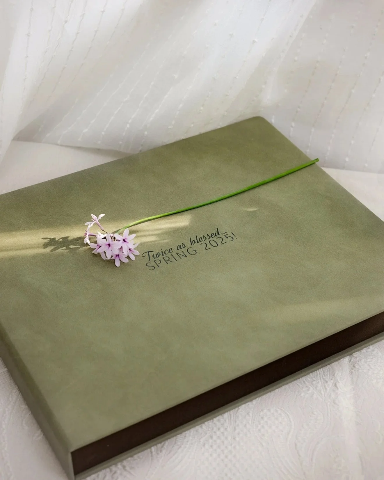 Luxury Photo album created for a client, A green gift box with a pink and white flower on top, with the words 'Twice as blessed... SPRING 2025!' written on it.