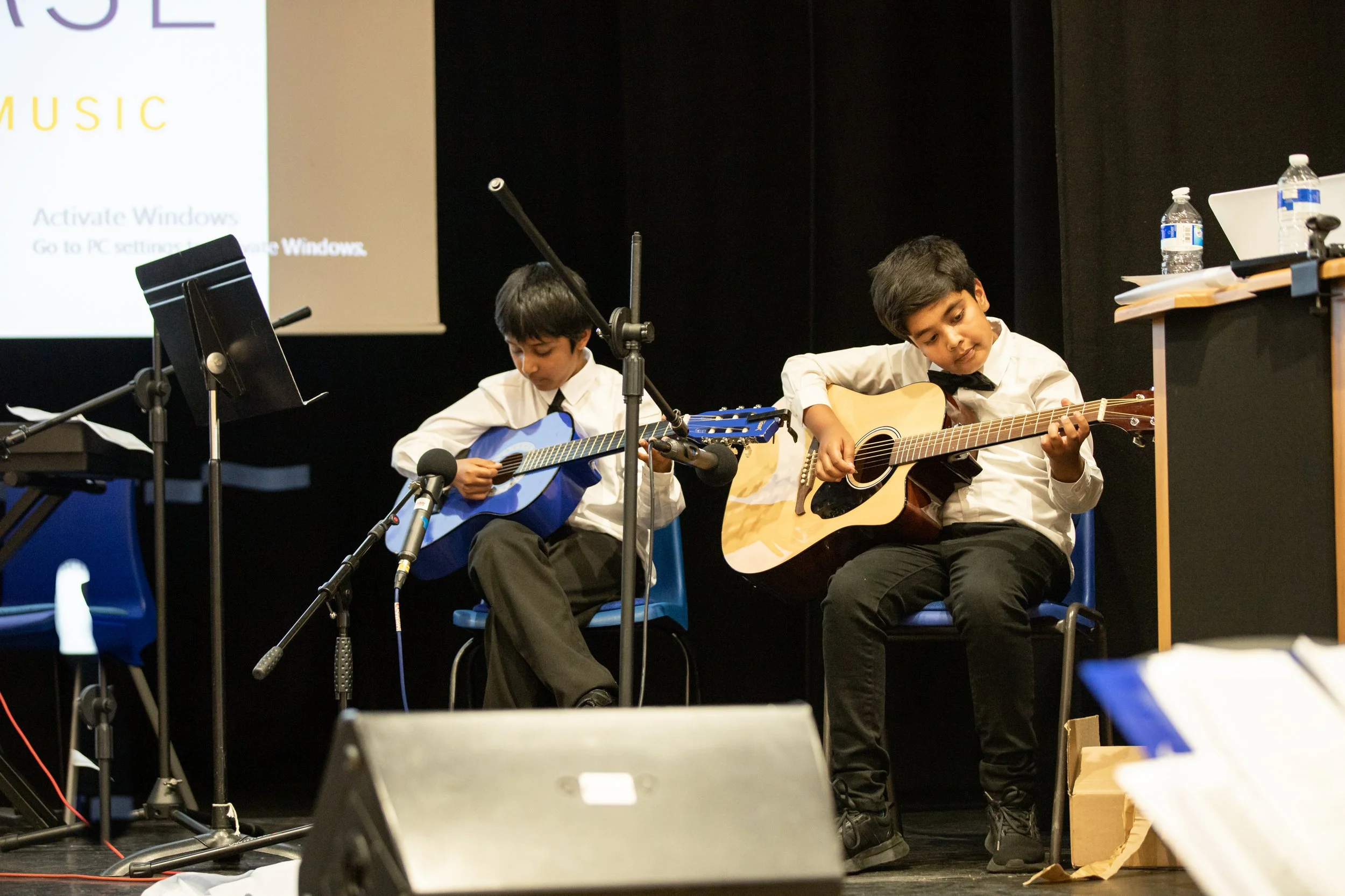 Two young boys playing acoustic guitars on stage, at music event captured by Berkshire event photographer
