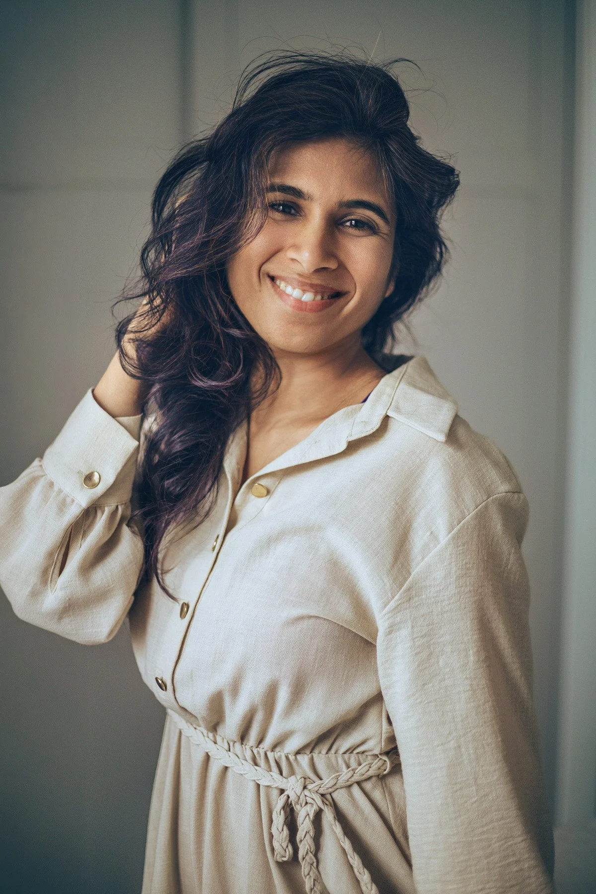 Woman with dark wavy hair smiling, wearing a beige dress, captured in a studio portrait by a photographer in Reading, Berkshire.