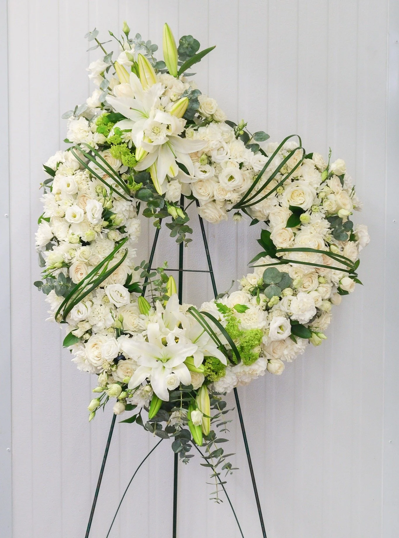 An elegant white sympathy heart wreath, thoughtfully designed with stunning white lilies and delicate lisianthus flowers. A peaceful and timeless expression of love, remembrance, and heartfelt sorrow.