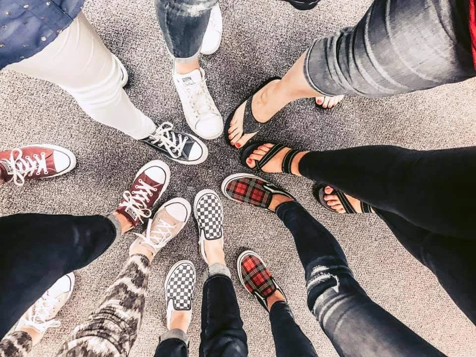 Group of people standing in a circle, showcasing their different footwear including sneakers, sandals, loafers, and patterned shoes.