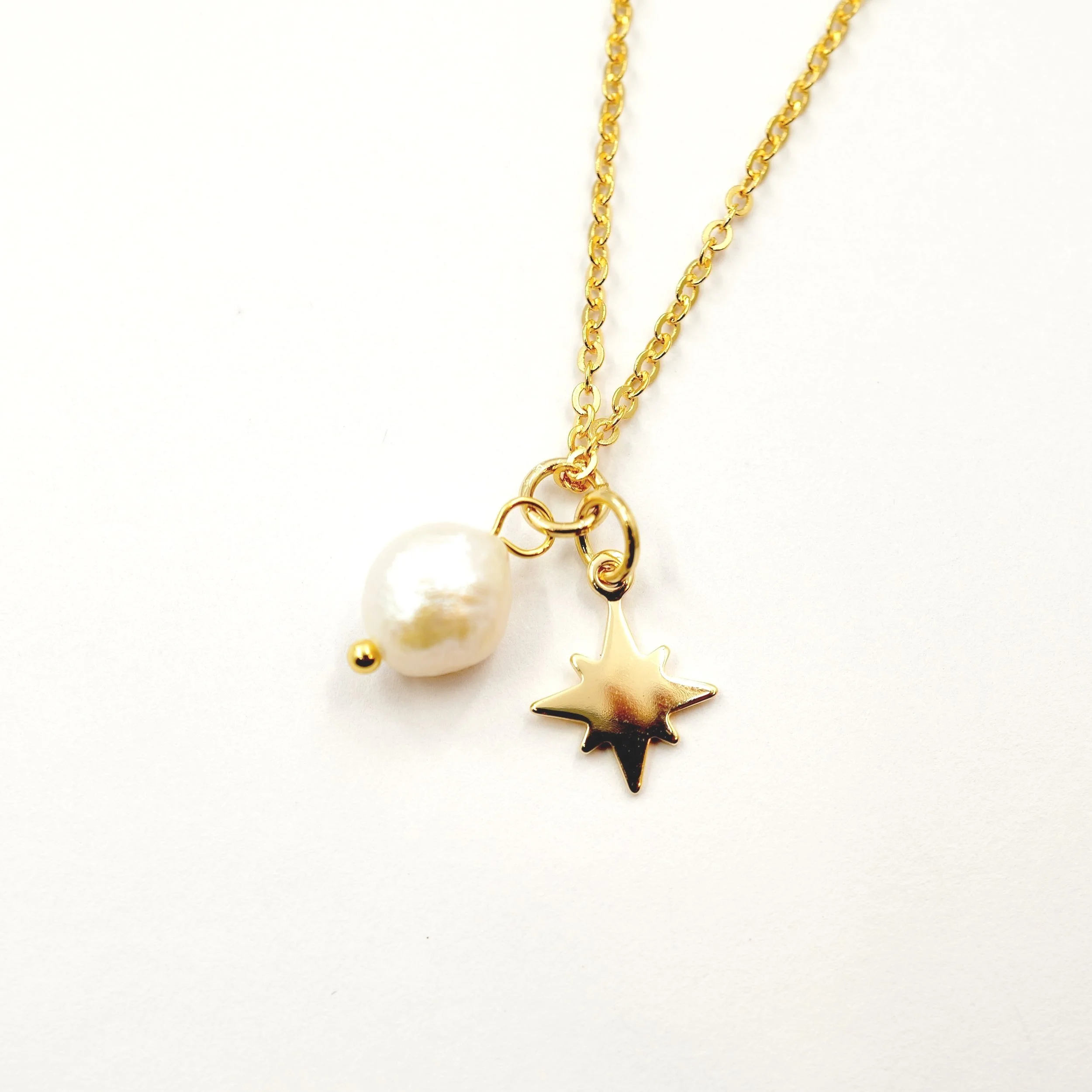 Gold necklace with a pearl pendant and star charm on white background.