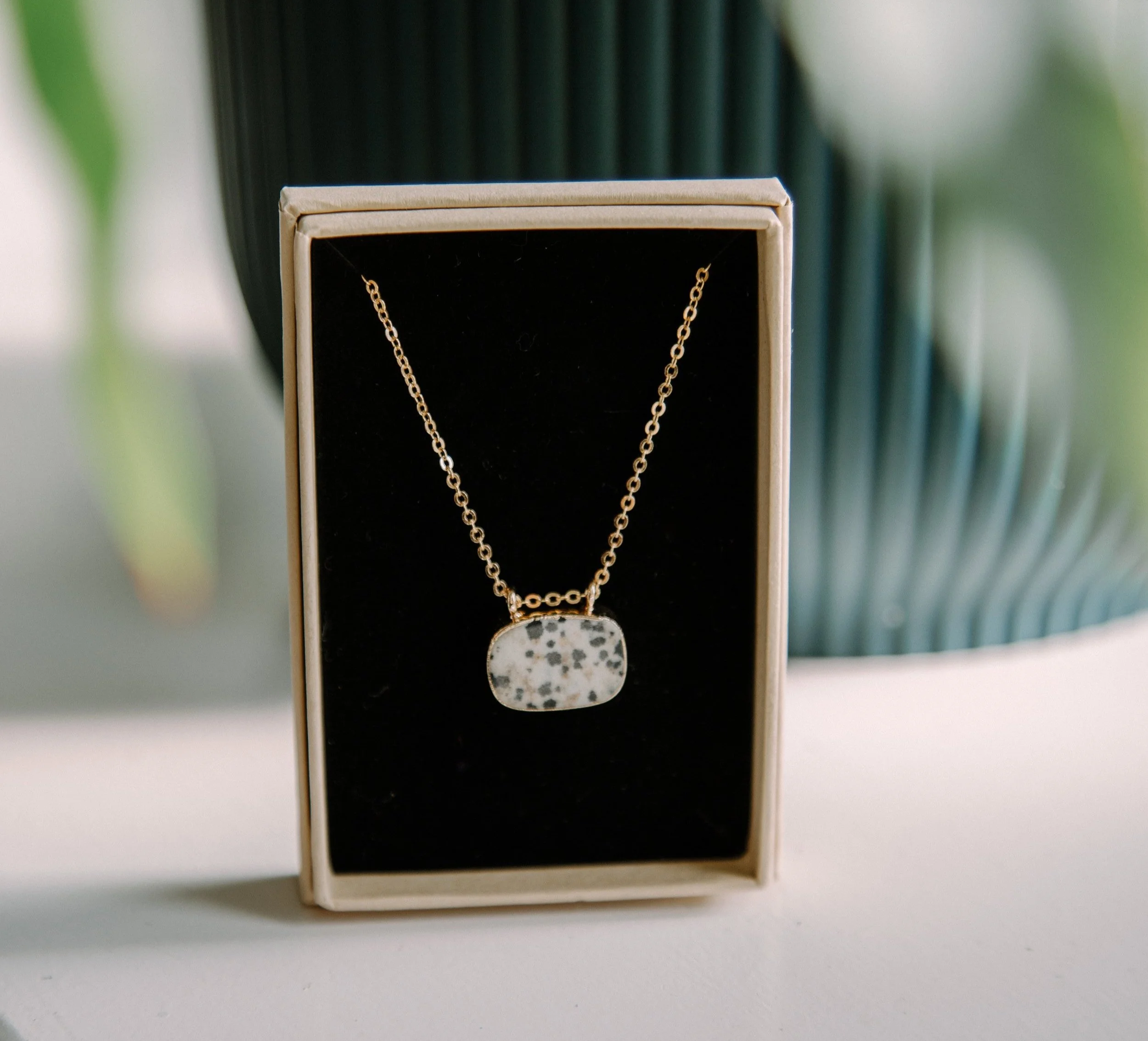 Gold chain necklace with a rectangular pendant in a display box, with a spotted stone design.