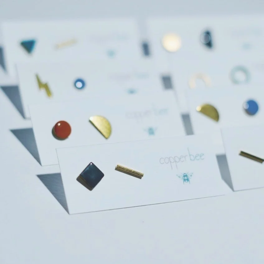 Assorted geometric earrings by Copper Bee displayed on white cards.