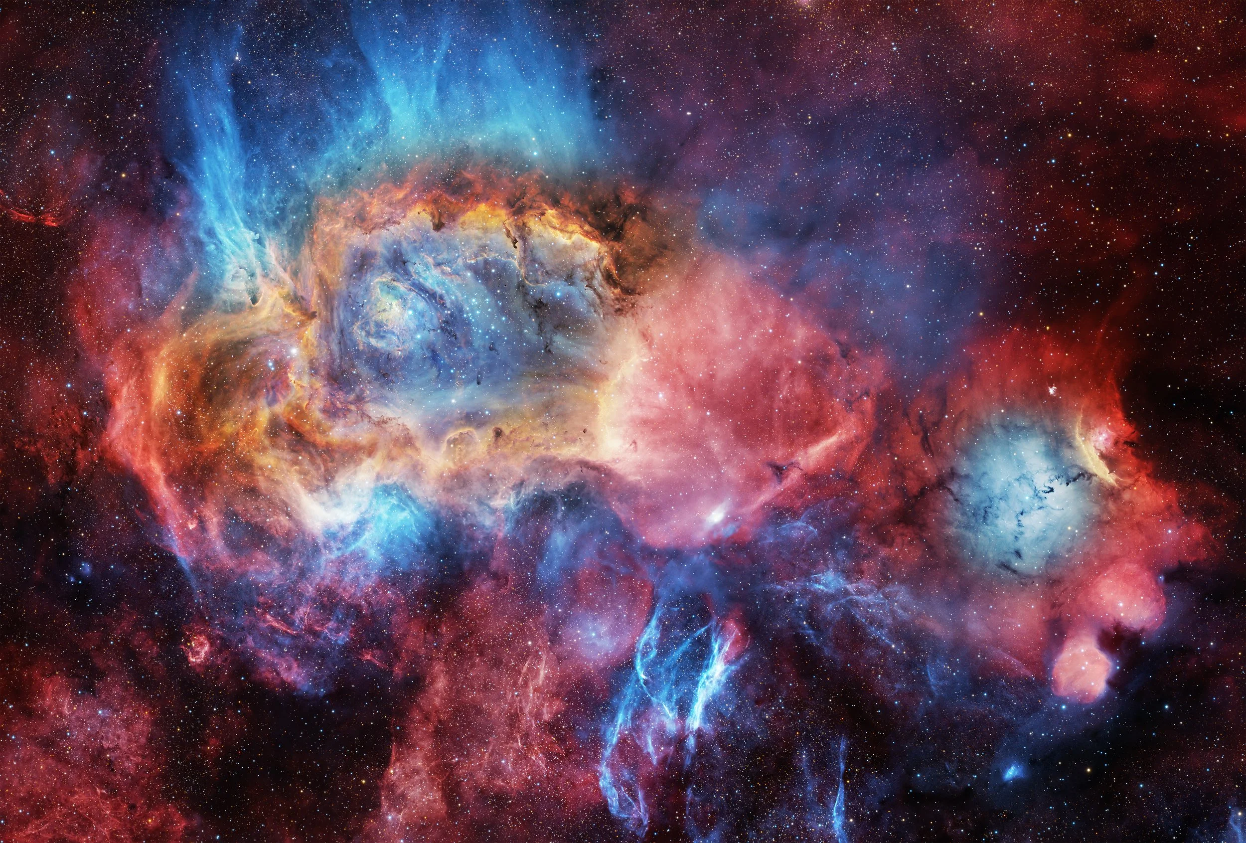A colorful wide-field image showing the Lagoon Nebula and Trifid Nebula surrounded by glowing gas and dark dust, with faint supernova remnant filaments woven through the star-filled Milky Way background.