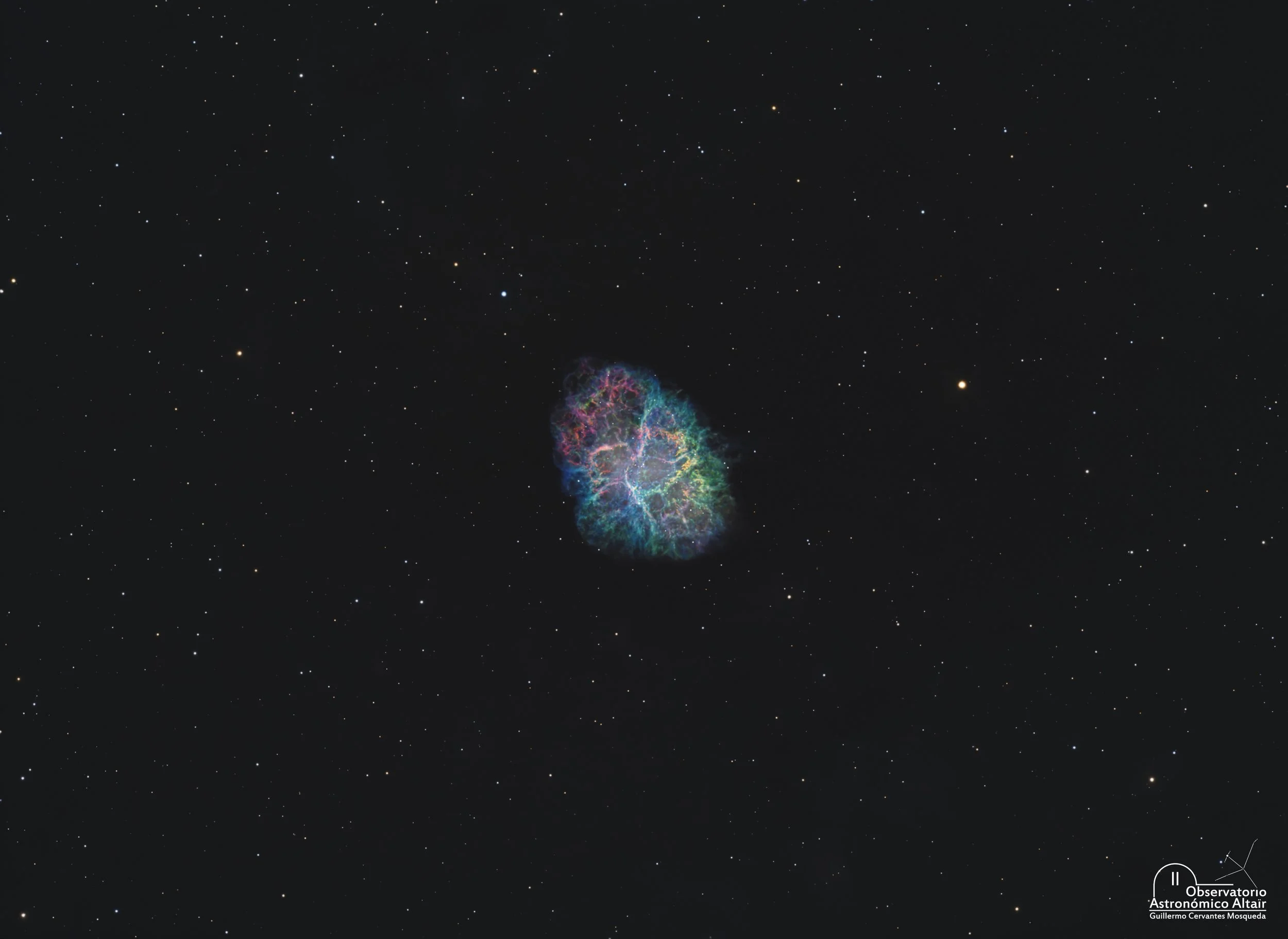 A Hubble Palette image of the Crab Nebula, showing a compact, oval shaped supernova remnant filled with intricate blue, green, and red filaments, set against a dark, star filled background.