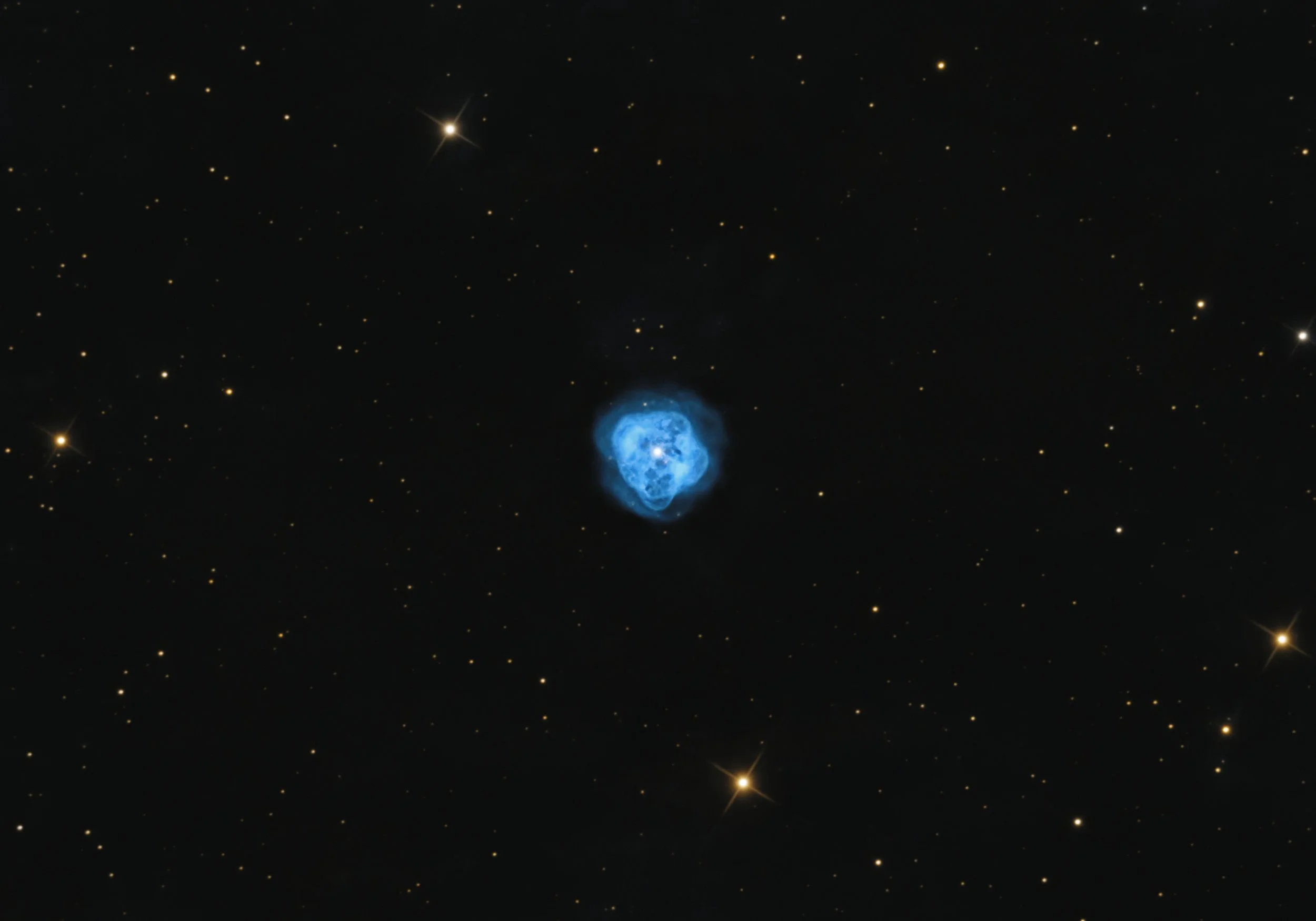 Blue planetary nebula NGC 1514 with a rounded, translucent glow surrounded by numerous golden and white background stars, photographed from New Delhi, India.
