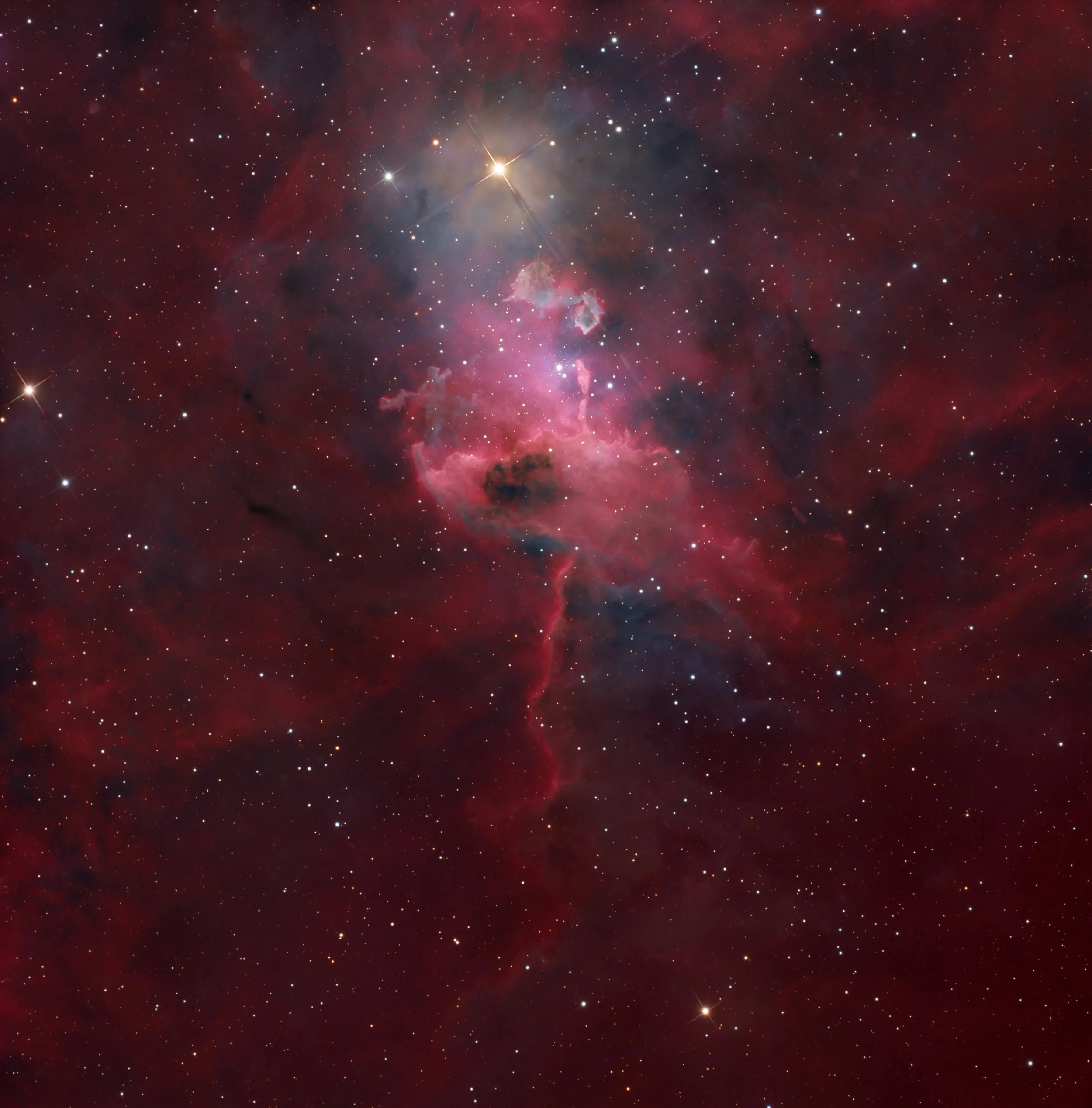 The Spider Nebula IC 417 glowing in deep red hydrogen light, with dark dust lanes and a bright central star illuminating swirling gas in Auriga.