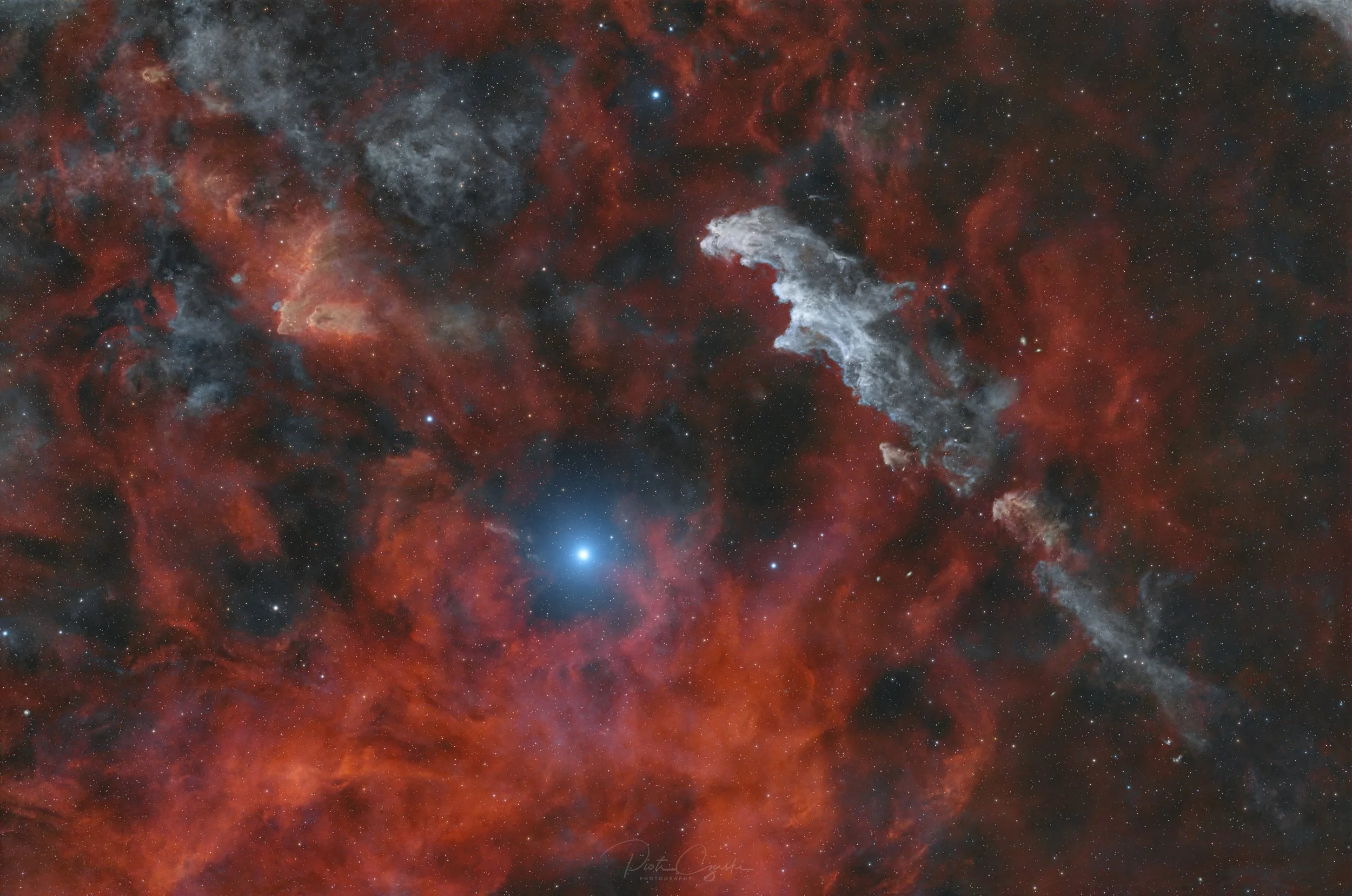 Wide field astrophotography of the Witch Head Nebula, a faint blue reflection nebula near Orion, surrounded by dark dust clouds and subtle red hydrogen emission.