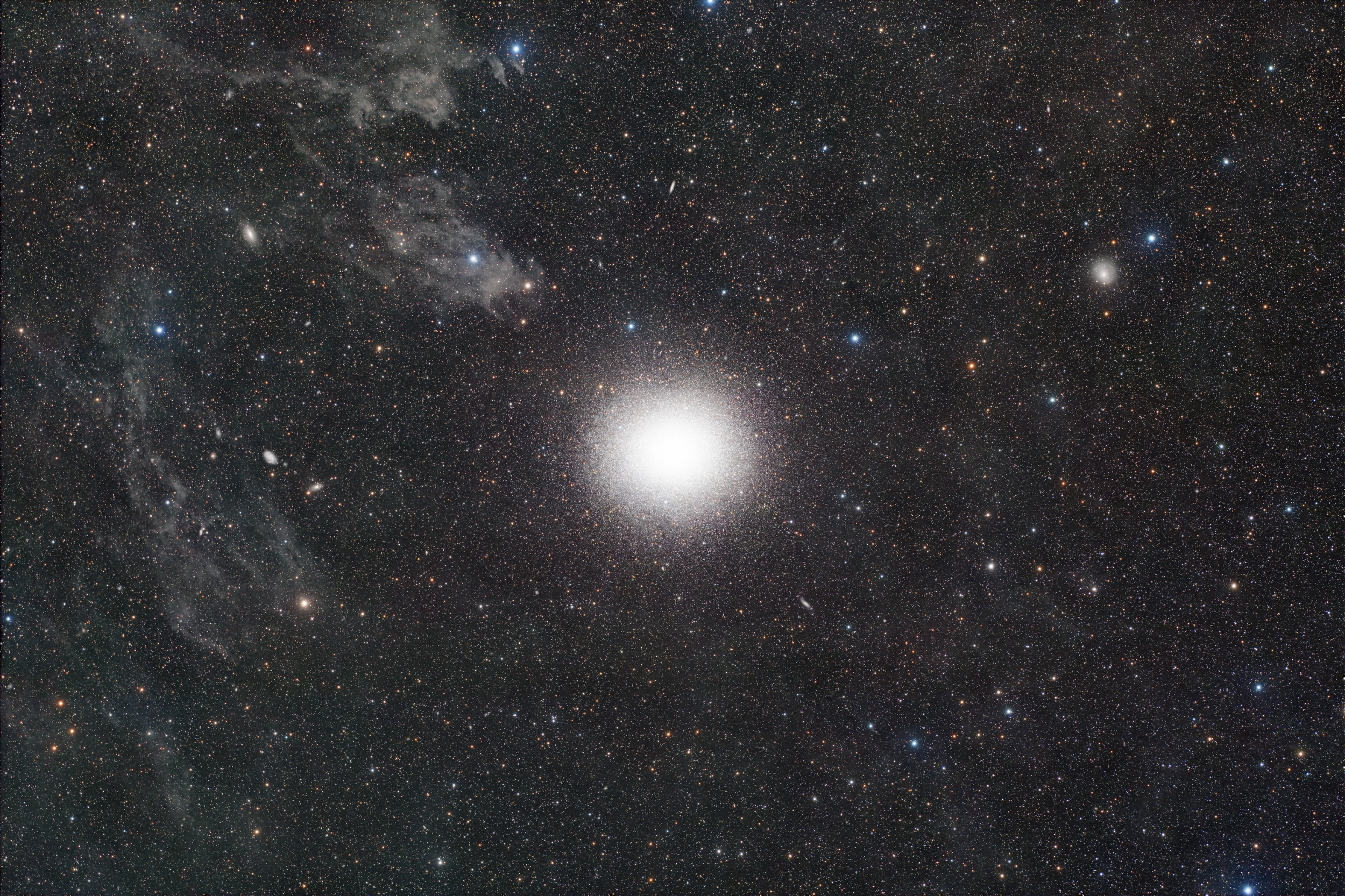 NGC 5139 Omega Centauri globular cluster with a brilliant dense core surrounded by millions of stars against a rich Milky Way star field and faint background galaxies.
