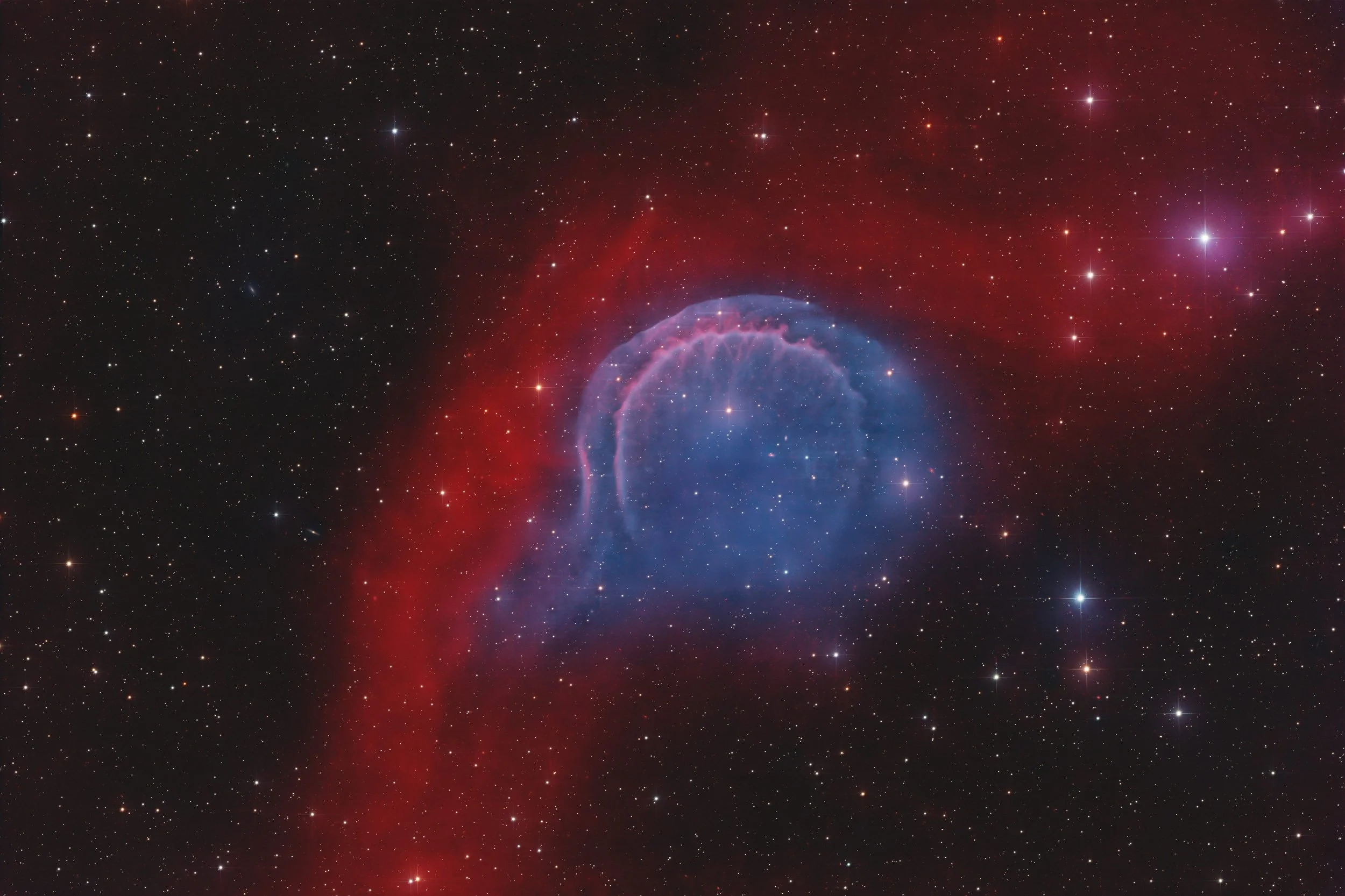 A faint, ghostly blue planetary nebula shell surrounded by red hydrogen emission clouds and a dense star field, showing the highly evolved remnant HDW 3 blending into the interstellar medium.