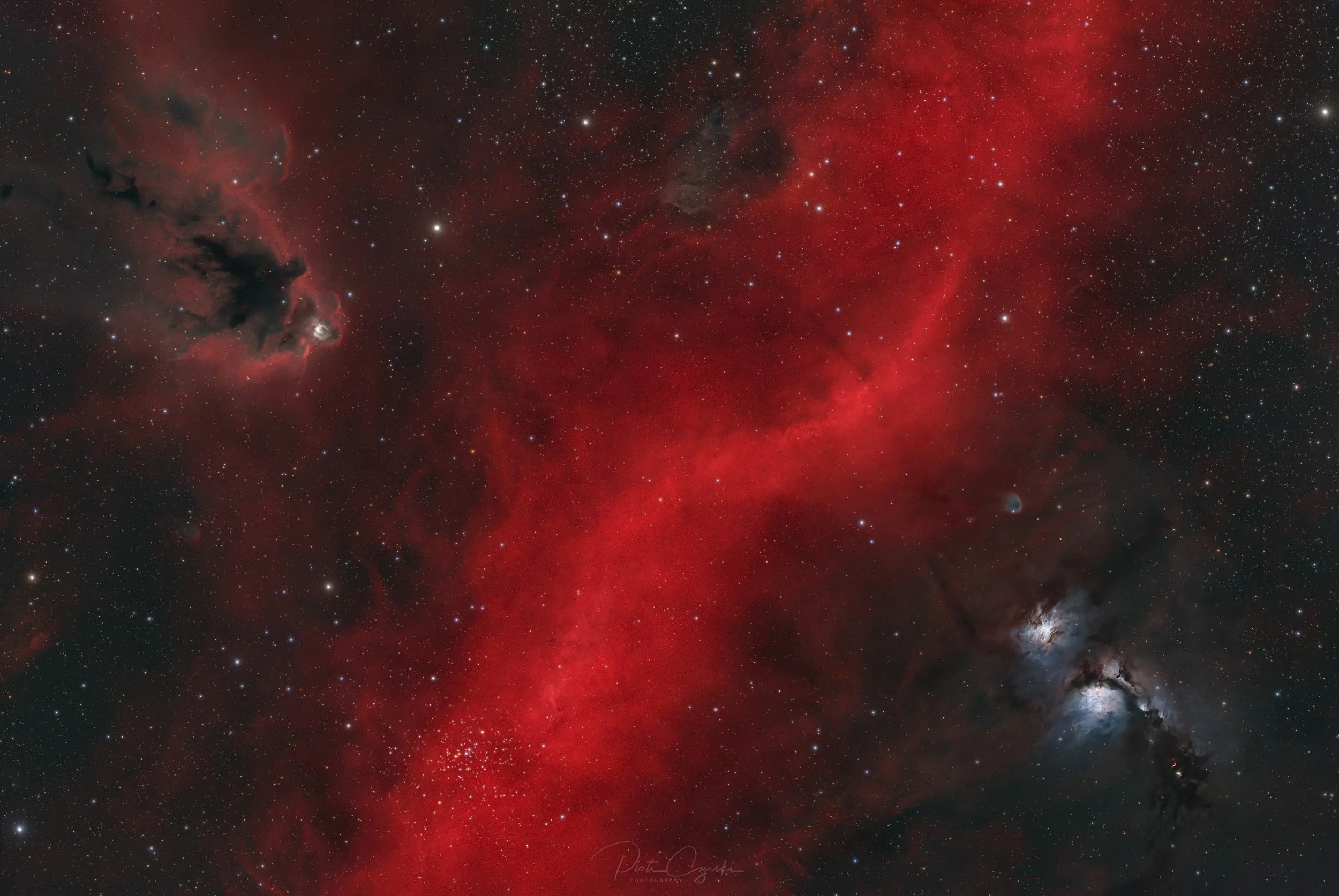 A wide-field HaRGB image of Barnard’s Loop showing bright red hydrogen arcs wrapped around dark dust clouds and blue reflection nebulae including M78 and LDN 1622 against a dense star field.