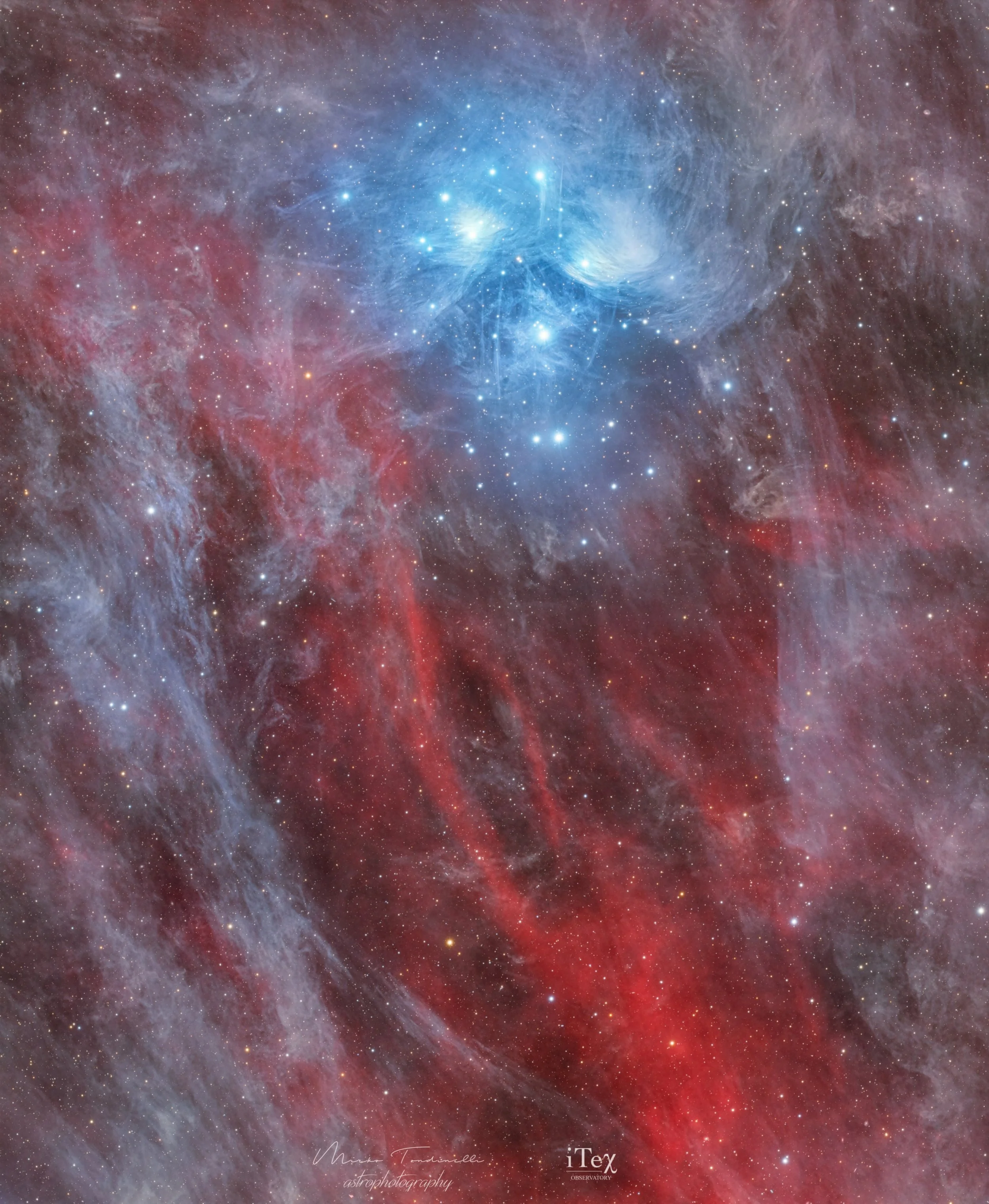 Wide-field astrophotography image of the Pleiades star cluster with bright blue reflection nebulae surrounded by wispy red and gray interstellar dust clouds against a dense star field