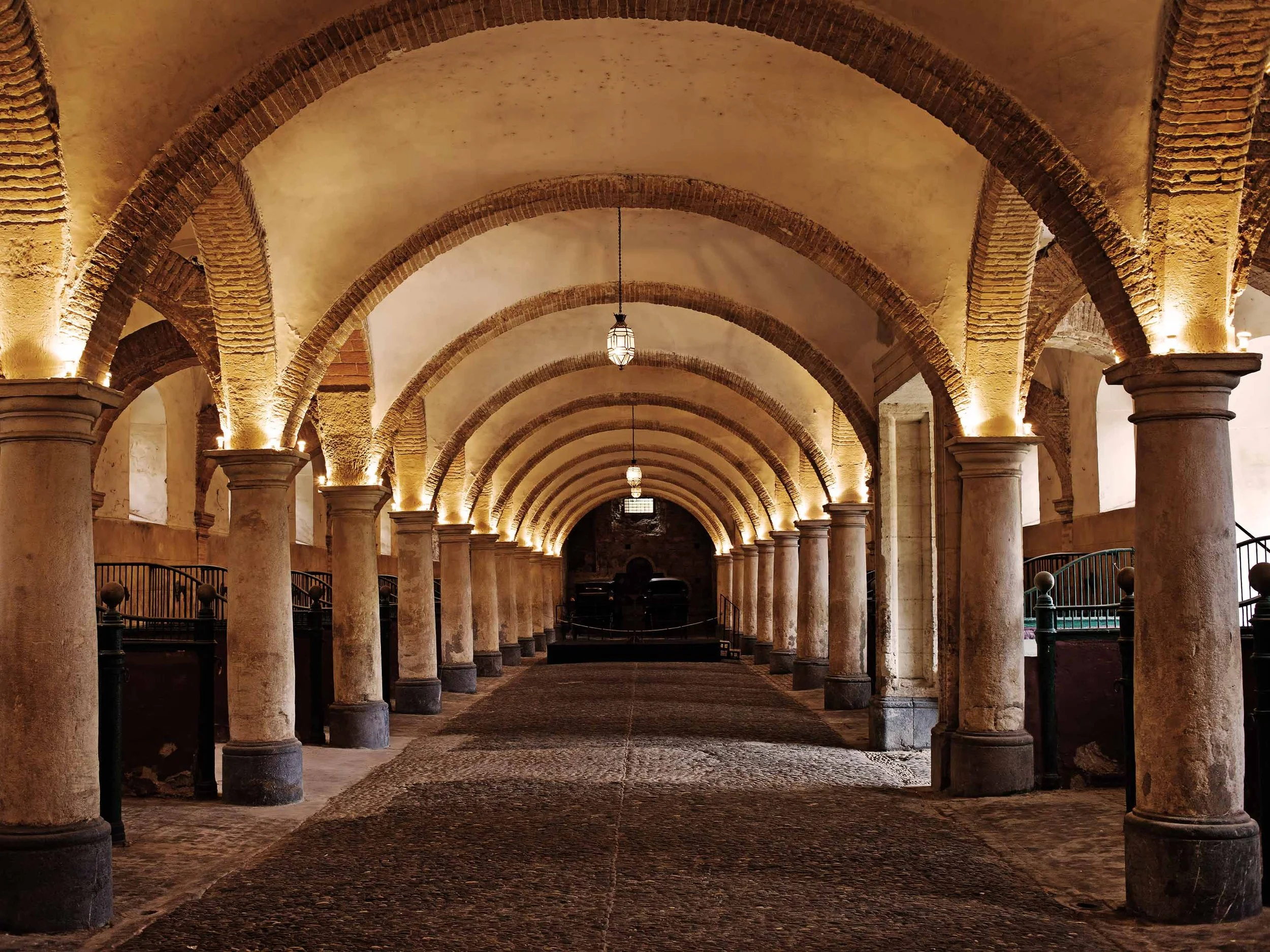 Image of a beautiful stable with warm lighting and stone arched architecture