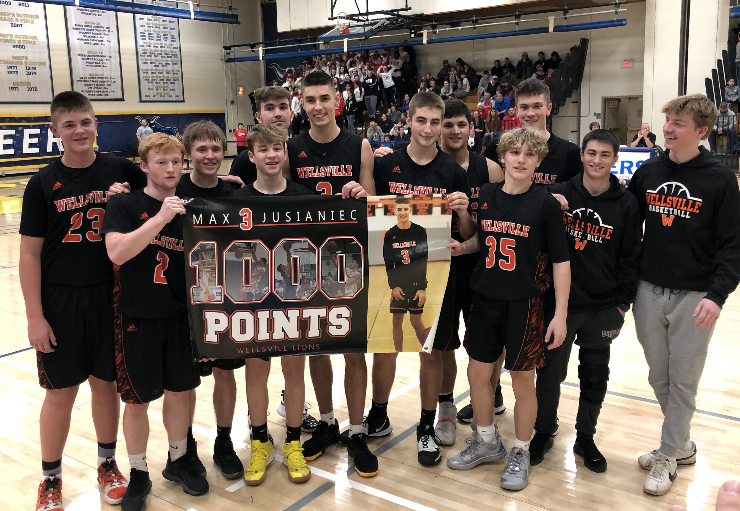  In the beginning stages of the fourth quarter, Jusianiec, middle, eclipsed the 1,000 point marker of his career. He poses with a celebratory poster marking his milestone alongside his teammates during a break in the action of Friday’s contest agains