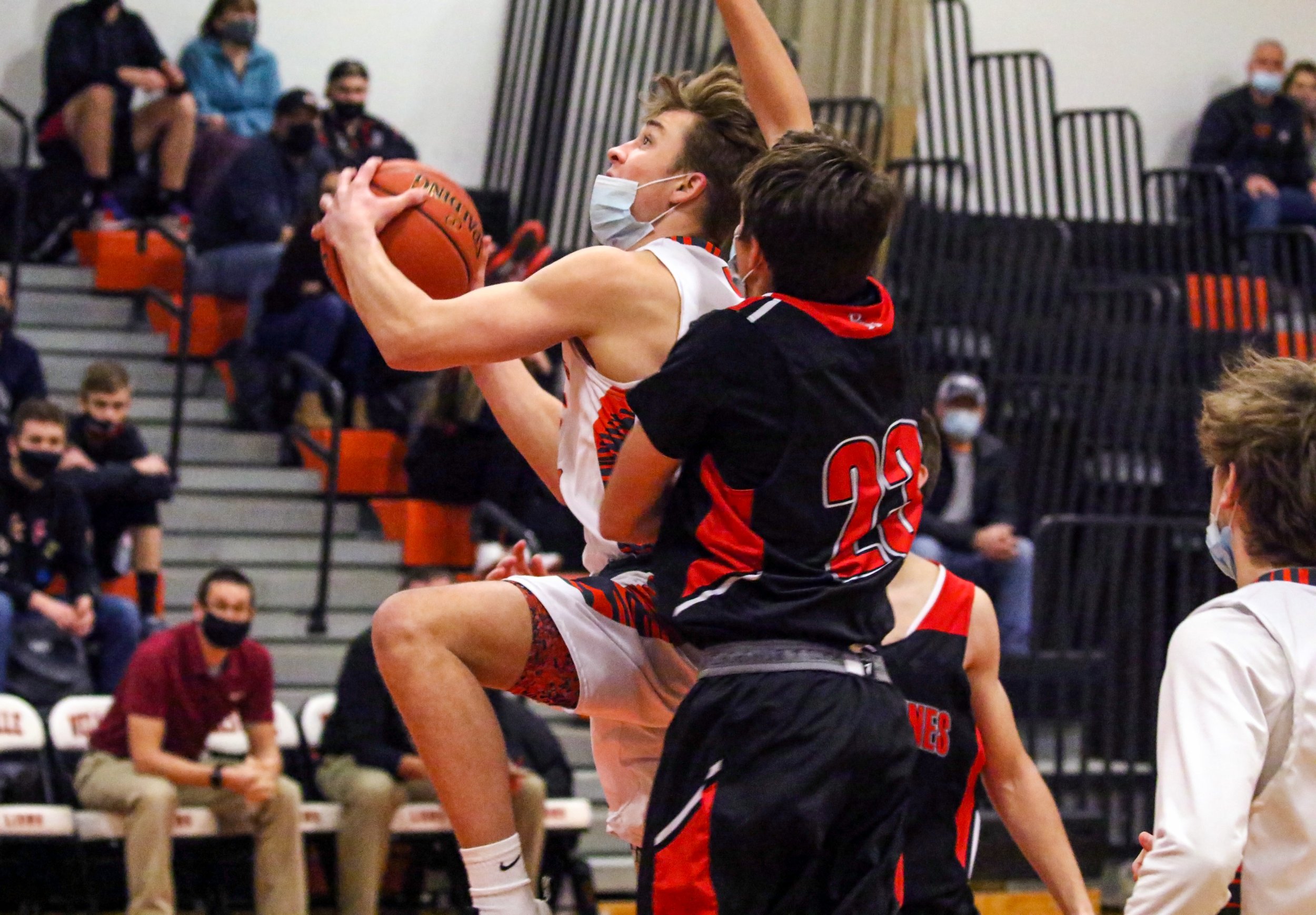  Wellsville senior Eli Schmidt, middle, goes up for the basket while under pressure from the defense of Bolivar-Richburg  junior Evan Pinney (23) during Tuesday night’s home contest in Wellsville. [Chris Brooks/WellsvilleSports.com] 