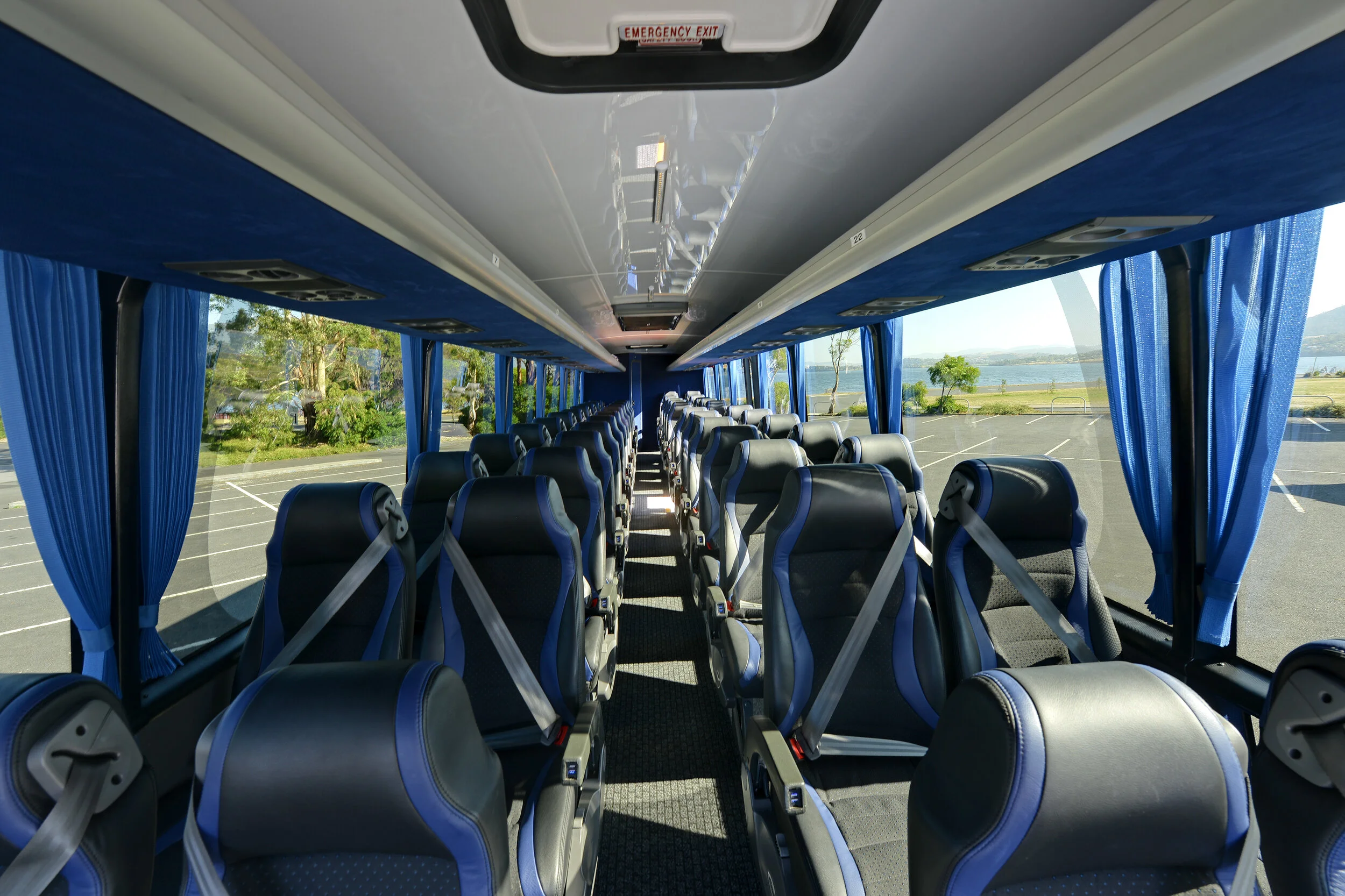 Interior of an empty tour bus with blue seats and curtains, showing seat belts and panoramic windows.