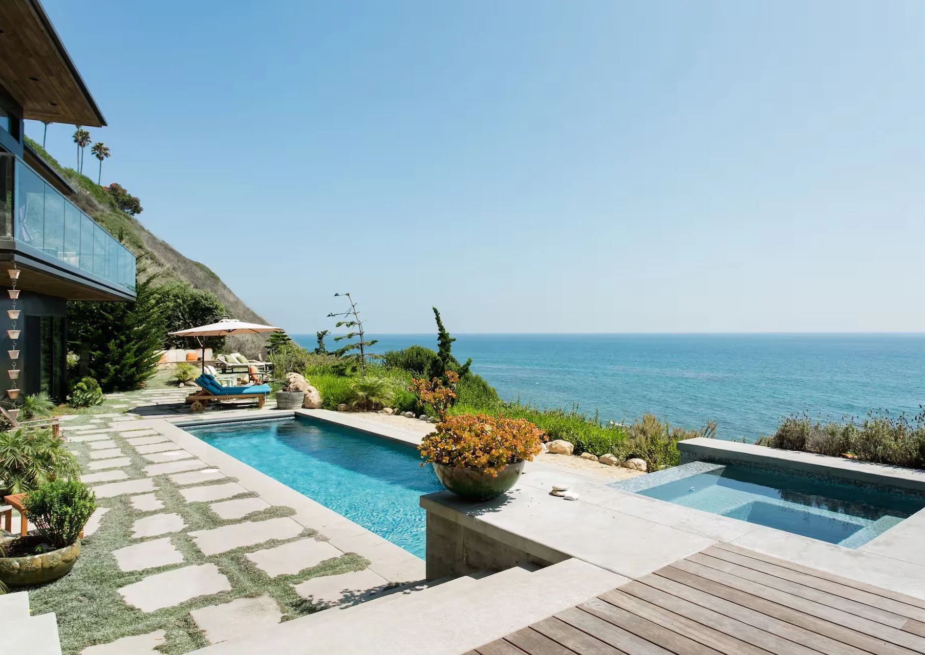 Luxury backyard with swimming pool, hot tub, lounge chairs, umbrella, and ocean view.