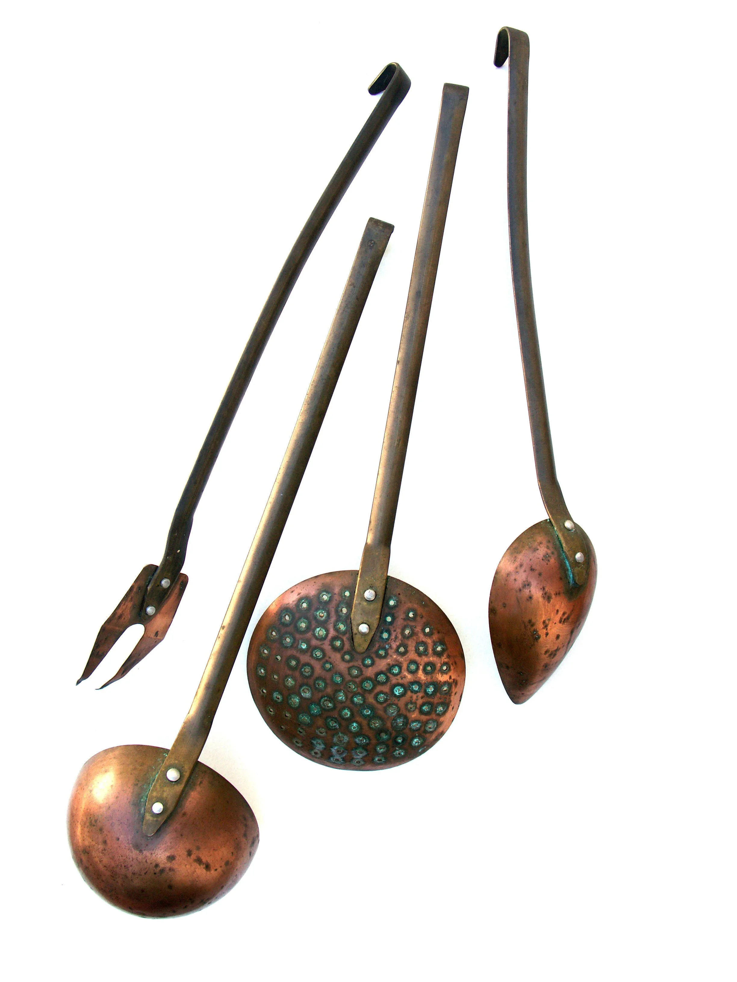 Set of four vintage copper or bronze kitchen utensils with darkened metal handles—two slotted spoons and two forks—arranged diagonally on a white background.