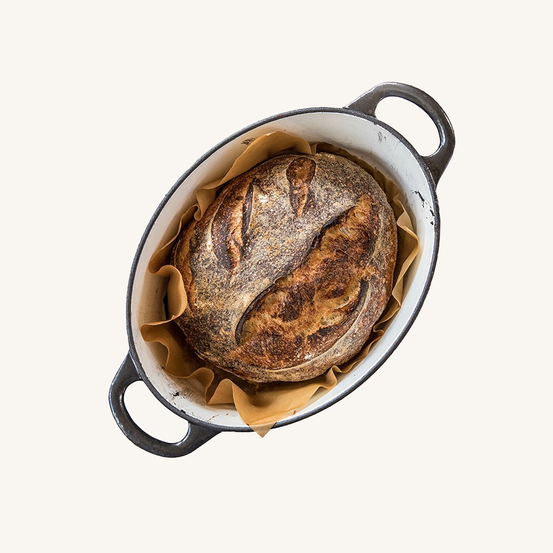 Baked bread loaf with a shark face design on top, in a white oval baking dish lined with parchment paper.